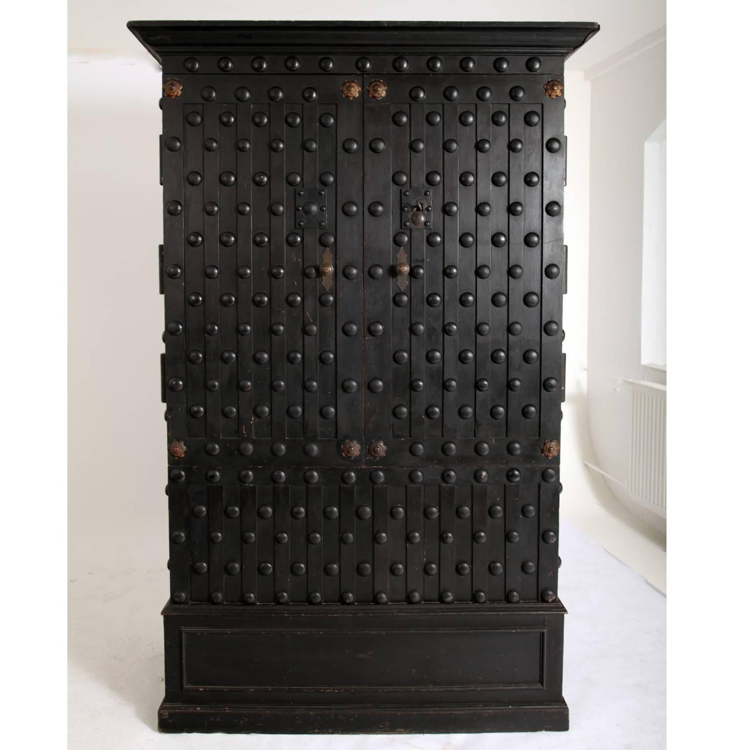 Unusual safe cabinet out of solid walnut with a slightly protruding cornice and a coffered base. The body is covered with wooden rivets that simulate the look of metal safes. Behind the doors are fourteen drawers and a large trunk compartment. The
