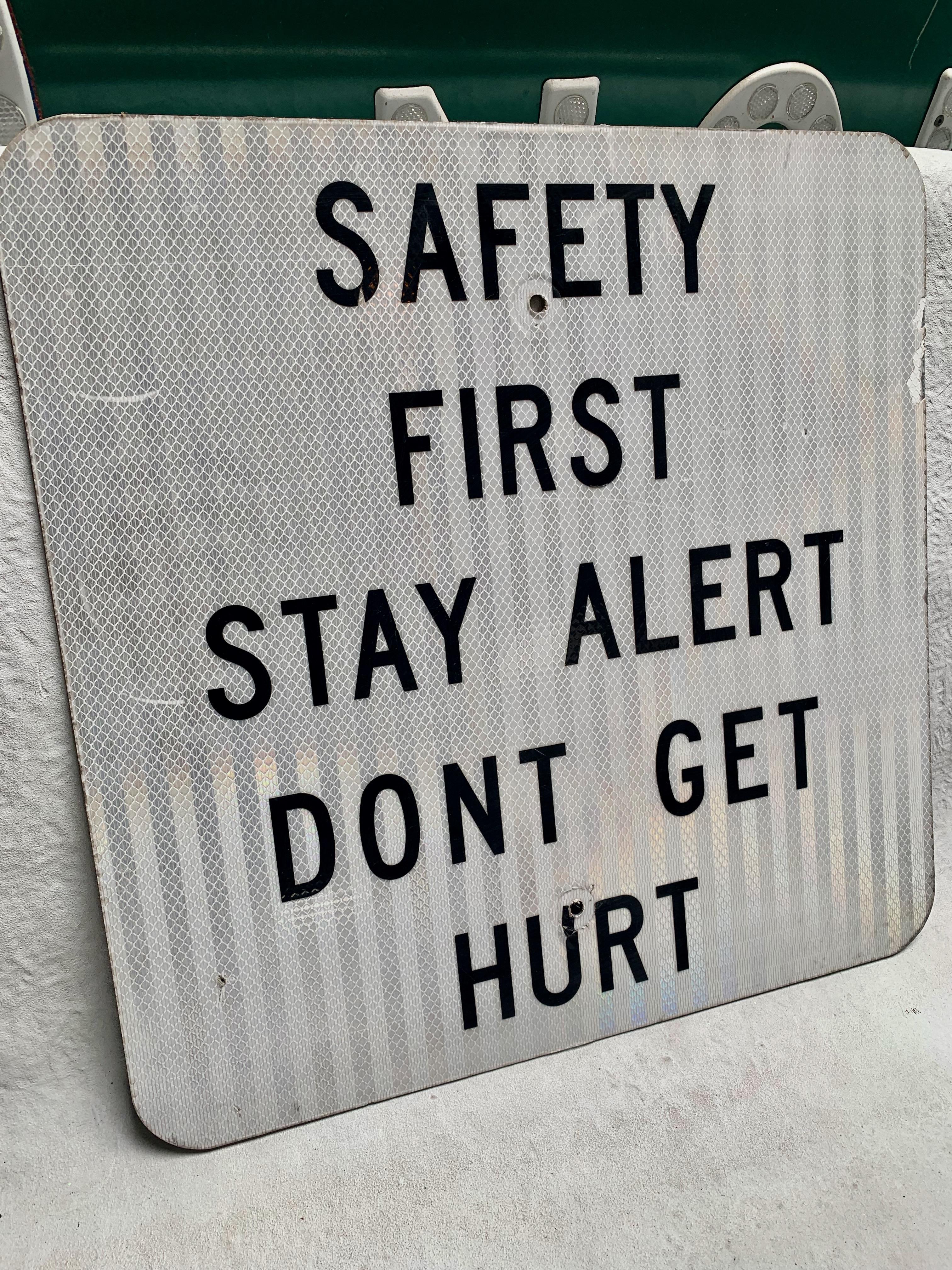 Interesting vintage highway sign. Safety First, Stay Alert, Don't Get Hurt. White reflective steel sign with black lettering. Great graphics. Super unusual sign.