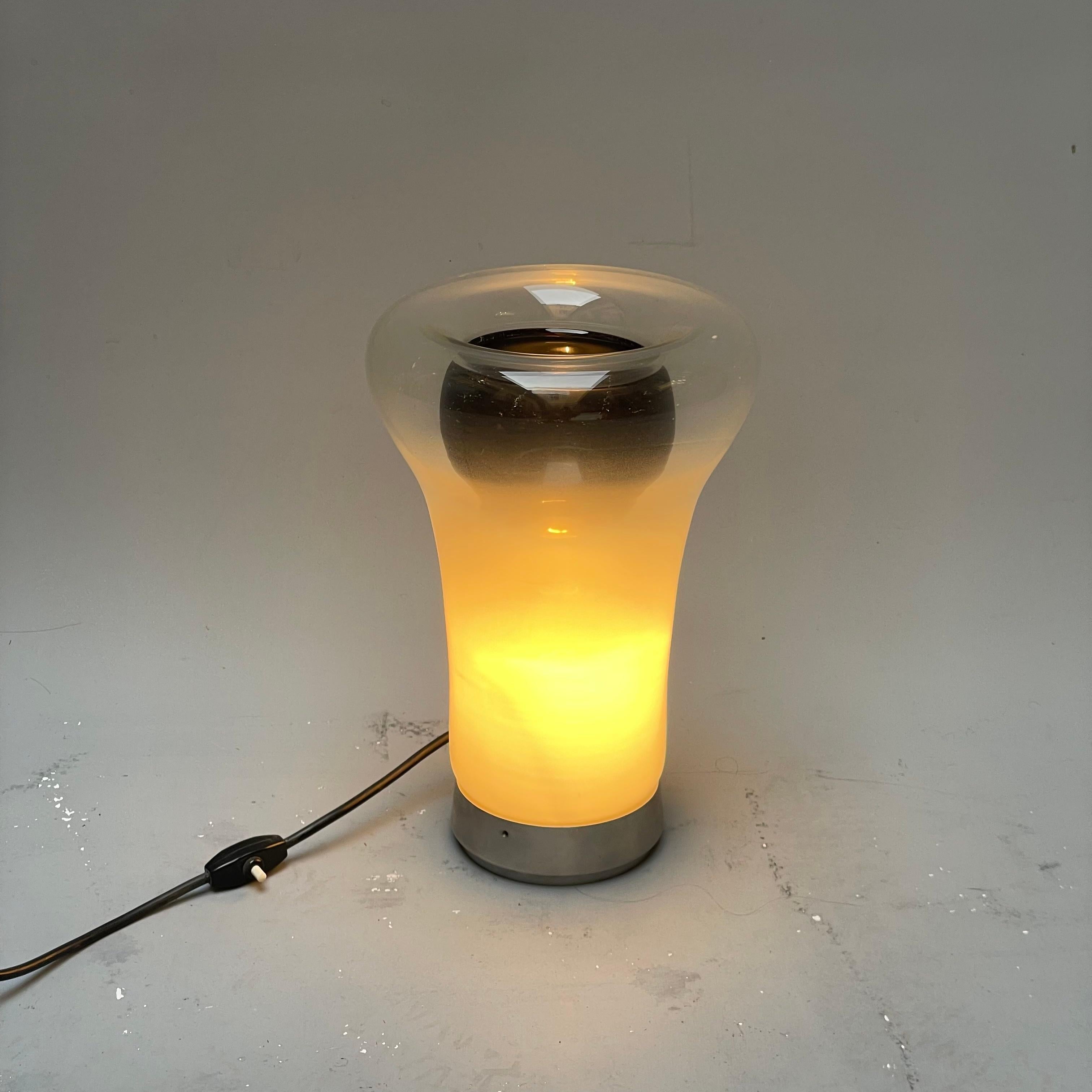 Designed by Angelo Mangiarotti and produced by Artemide in 1967, the lamp is made with a metal ring that supports a blown glass diffuser. Thanks to its shaded surface it can dim the light of the light source. The lamp is in very good condition to be