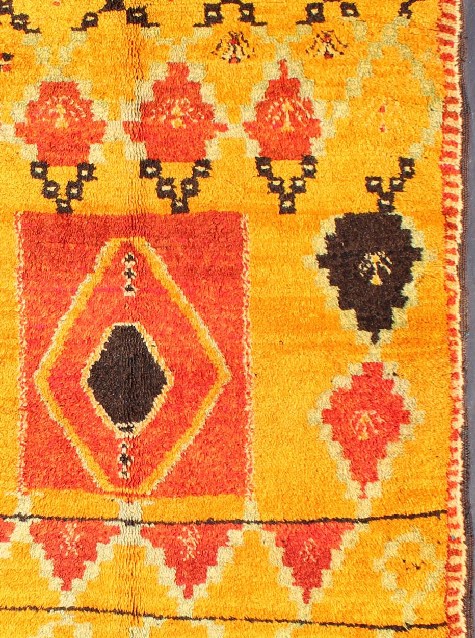 Measures: 4'4'' x 6'6''. 
Crafted in the mid- 20th century, this gorgeous Antique Moroccan Rug bears a body of saffron and soft orange and golden hues. Five rows of geometric patterns in a charcoal color are strung together and run the length of