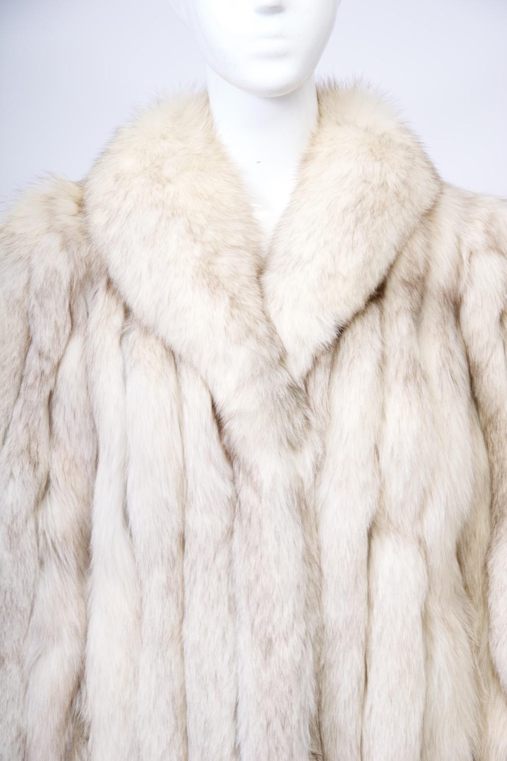 Vintage fox jacket featuring vertical skins joined by leather strips by renowned Saga company. The straight cut jacket boasts a shawl collar and hidden slash pockets, as well as fur hook closures. Hip length. On the interior, find a clean ivory