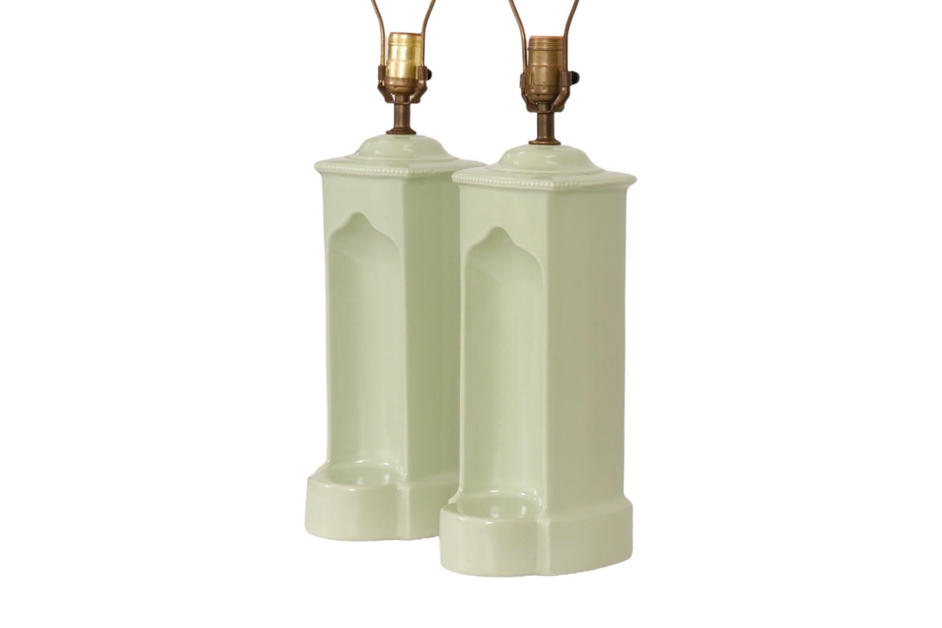 A pair of sage green ceramic table lamps made by Navis & Smith of Chicago, Illinois. Square bodies are trimmed with beaded edging around the top, stand on a rounded base and have a niche with a shelf in front. The maker's label is in the back, at