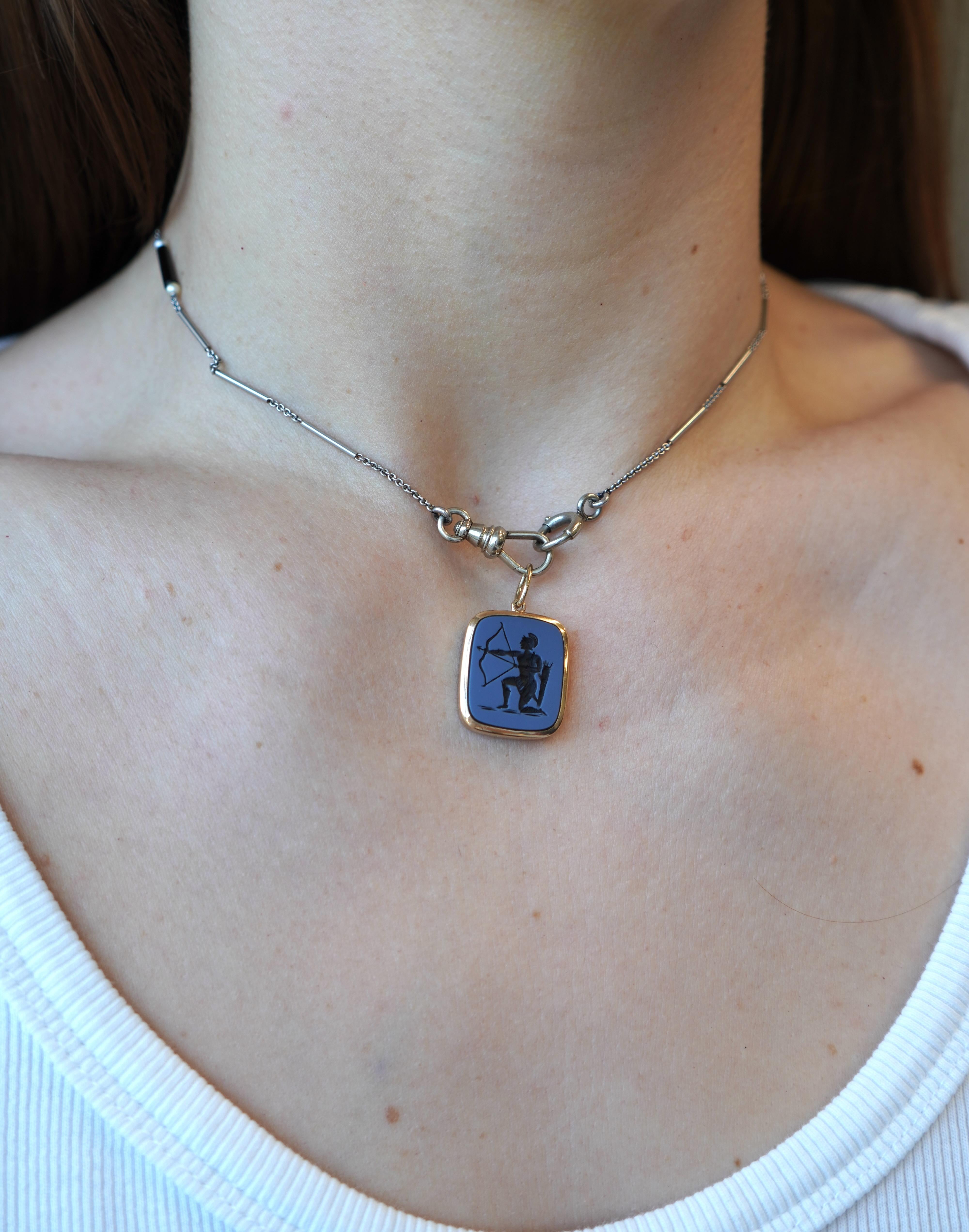 Questa collana antica combina una catena da orologio in platino con un ciondolo a forma di sagittario. La catena, risalente agli inizi del XX secolo, è realizzata in platino con perle naturali e accenti di onice nera, misura 11 pollici di lunghezza