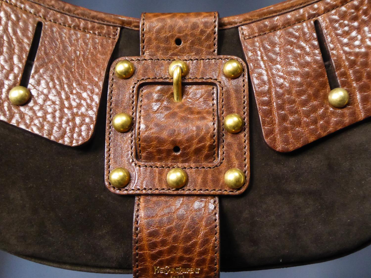 Circa 1990
France

Beautiful Saharienne bag in tawny leather and brown suede by  Yves Saint Laurent Rive gauche dating from 1995. Flap tabs and fake buckle studded with brass balls. Small strap with brass rings and  interior in brown satin with