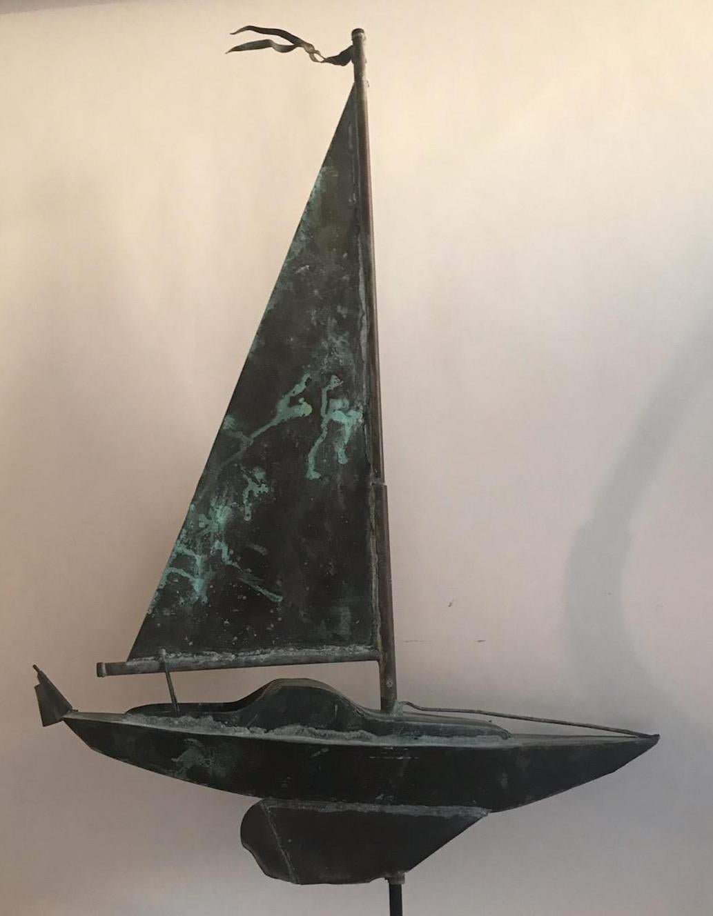 This smaller version sailboat weather vane from the 1930s has a fantastic aged patina. The sails have two nautical flags flying. It sits on a custom made cast iron base that is easy to remove if you want to mount on a roof top. Minor dings or dents