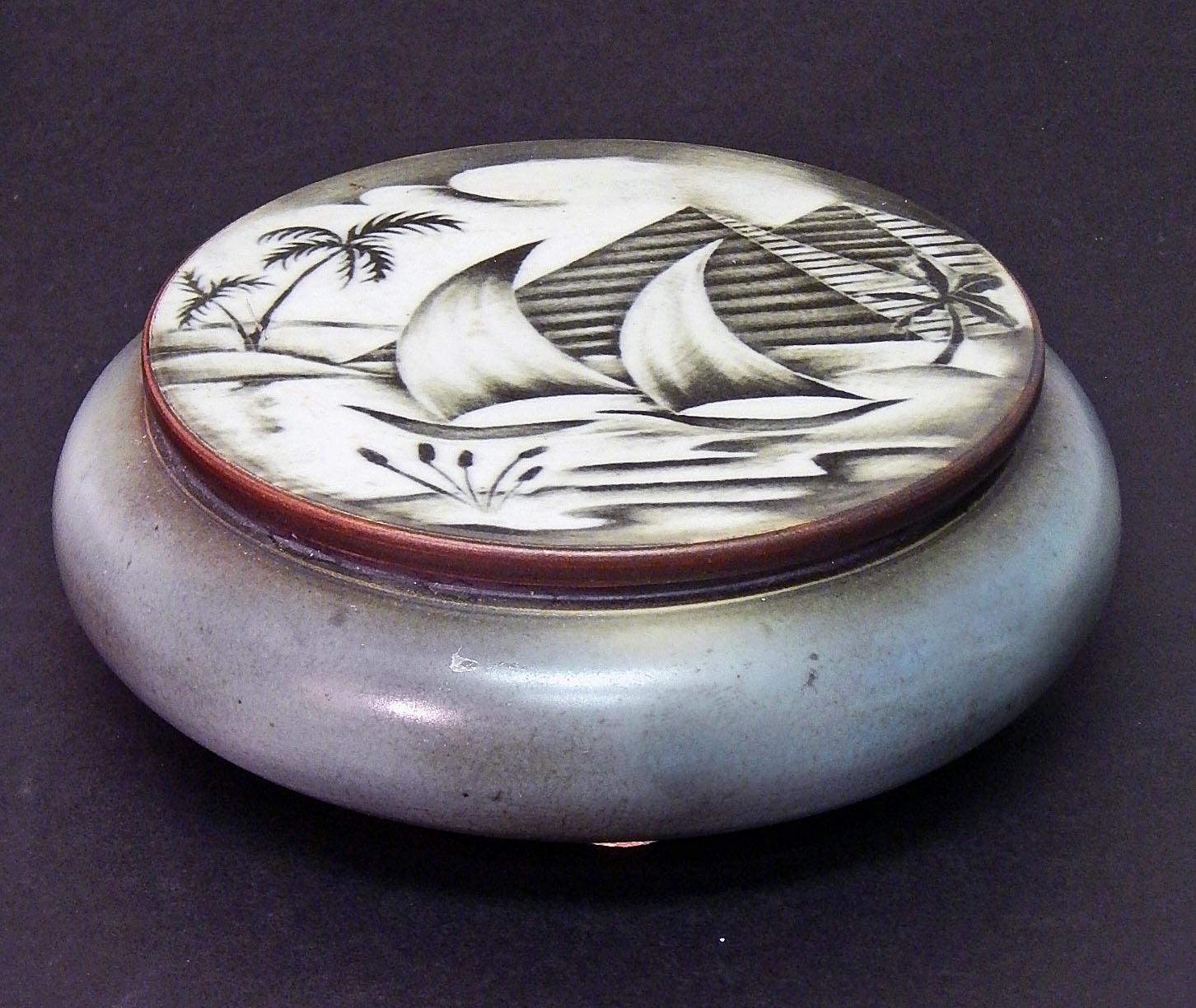 Striking and rare, this round covered Art Deco box depicts two traditional boats with sails on the Nile River, with two of the great Pyramids of Egypt in the background, and palm trees and reeds along the river's edge. This piece was designed by