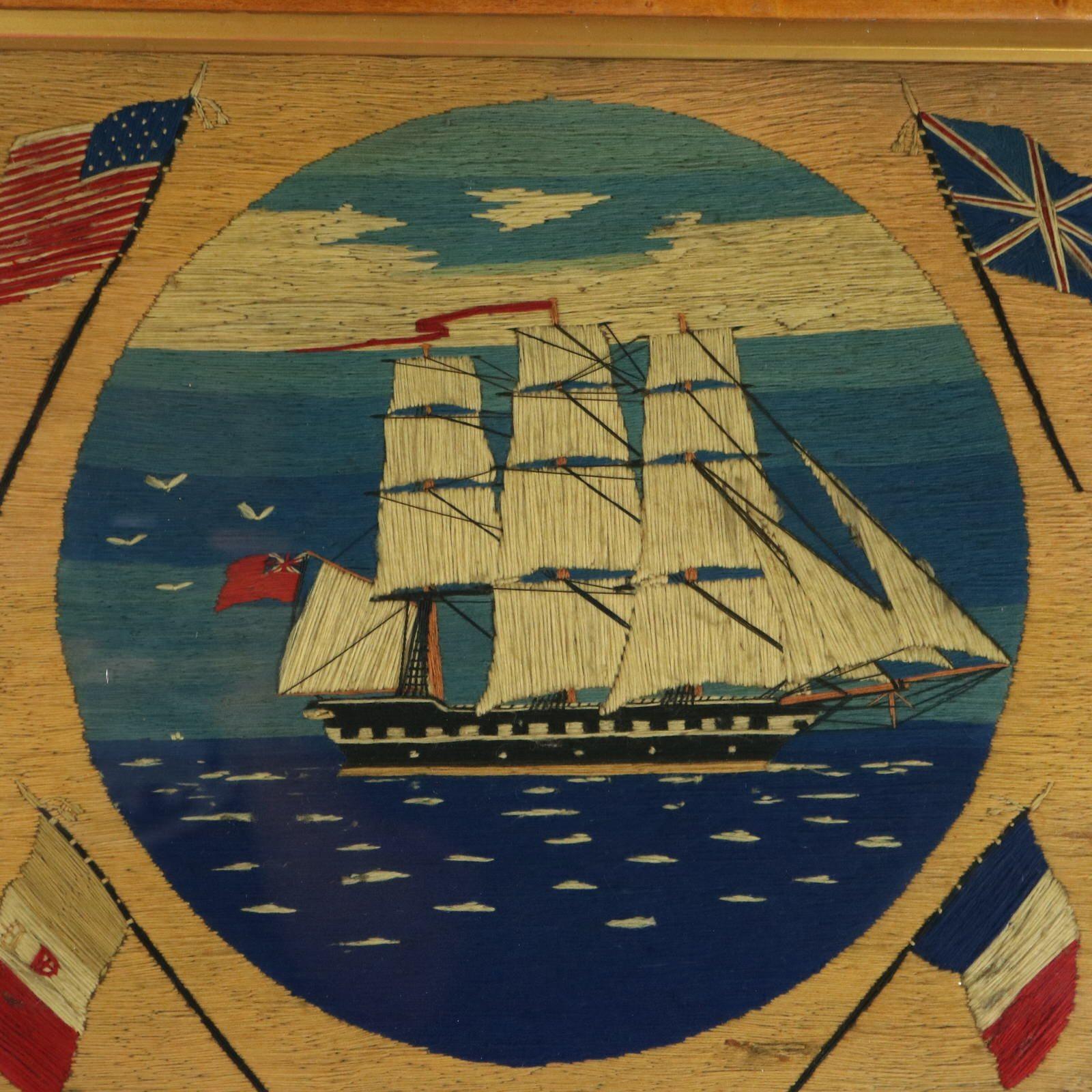 Sailor's Woolwork Embroidery Picture of a Ship surrounded by flags. Picture has a central panel depicting a three masted navy ship at sea. Flags in each corner - American, British, French and Italian (probably) flags. Framed in a maple veneer wooden