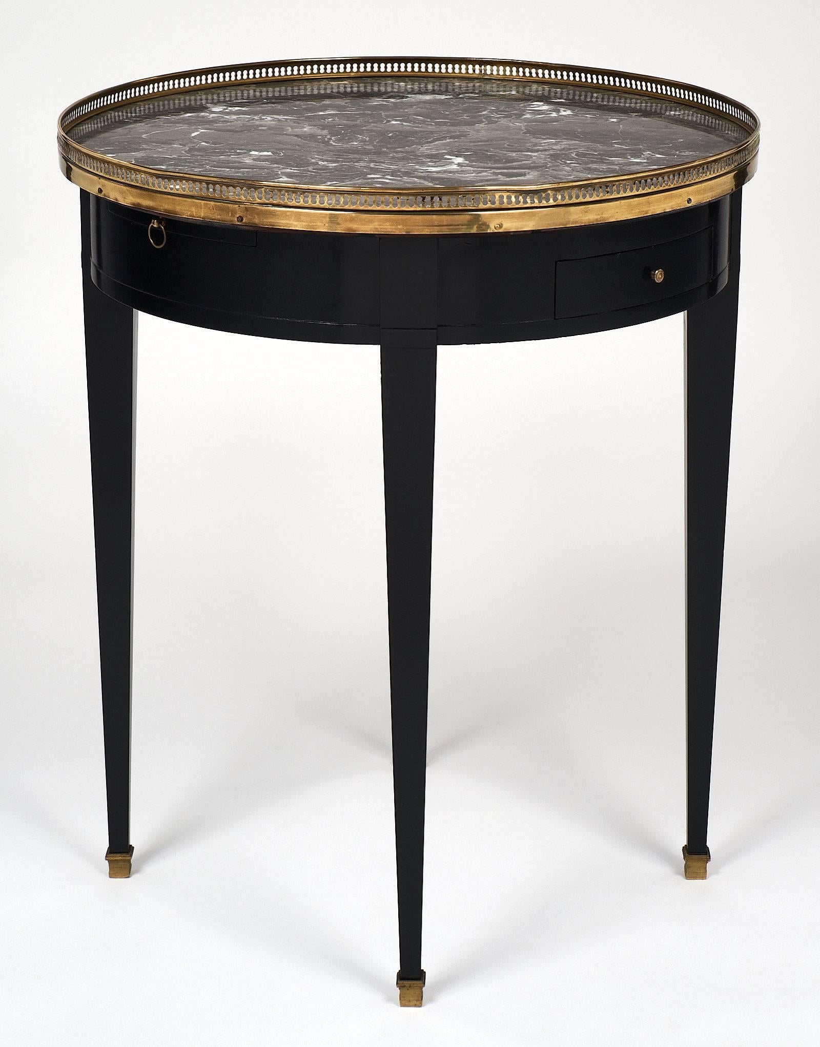 A charming antique Directoire style bouillotte table; ebonized finished with a lustrous French polish. This table features an intact Sainte Anne marble top, grey with white veining, and a hand-hammered open gilt brass gallery. There are also two