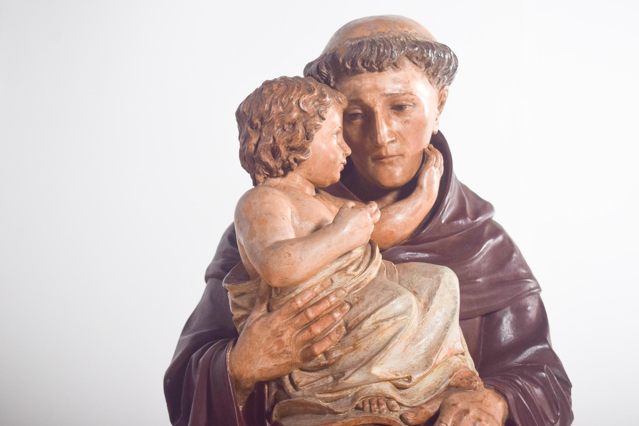 Sant'Antonio con il Bambino, scultura in ceramica. Sant'Antonio indossa il tradizionale abito francescano marrone, con il caratteristico cordone a tre nodi intorno alla vita. Il Bambino Gesù è avvolto in un leggero mantello e poggia su un libro, a