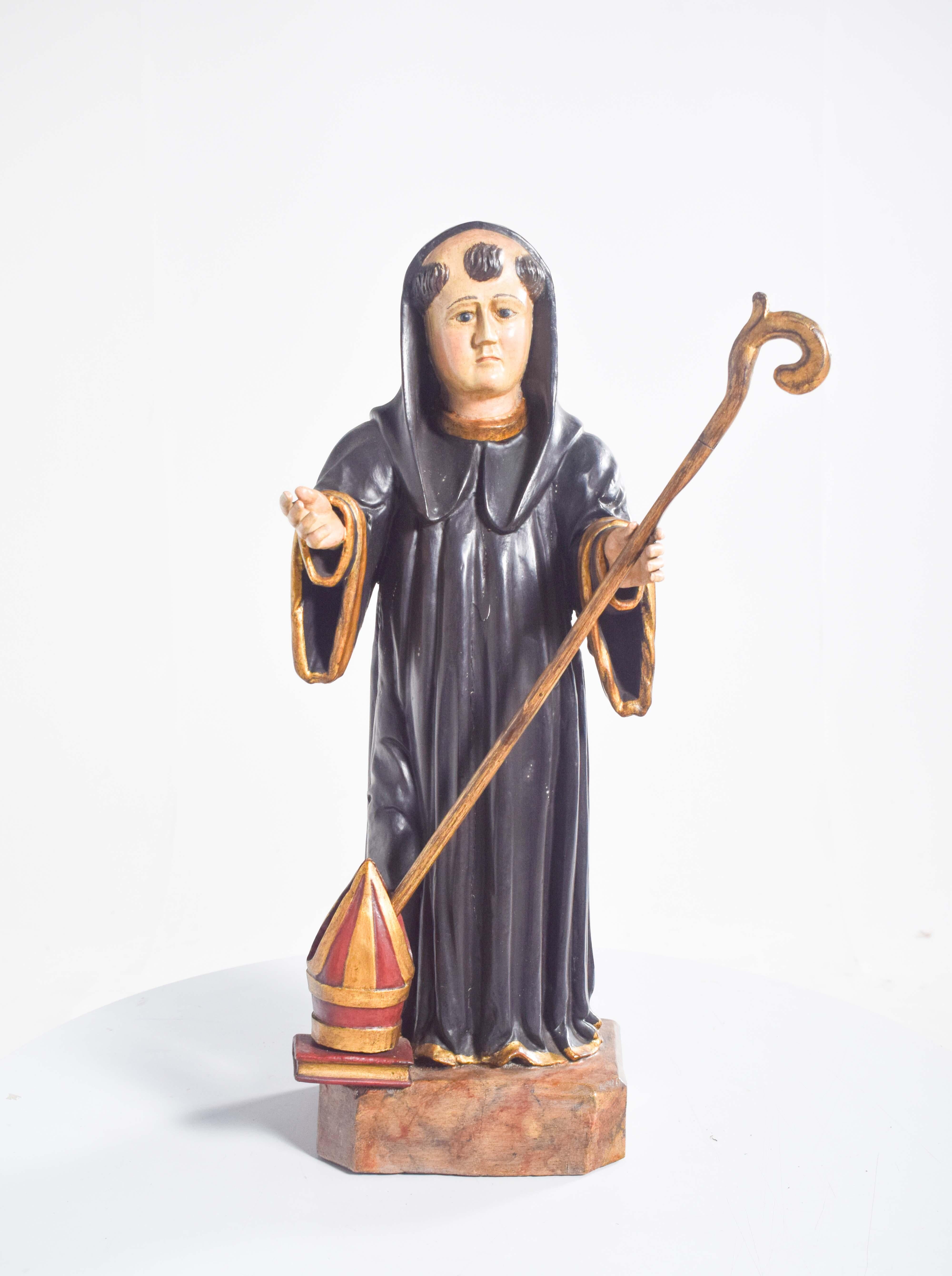 Questa scultura in legno splendidamente intagliata rappresenta San Benedetto, una figura di profonda importanza spirituale. Il santo è raffigurato con il tradizionale abito monastico nero, che simboleggia l'umiltà, la devozione e il suo ruolo di
