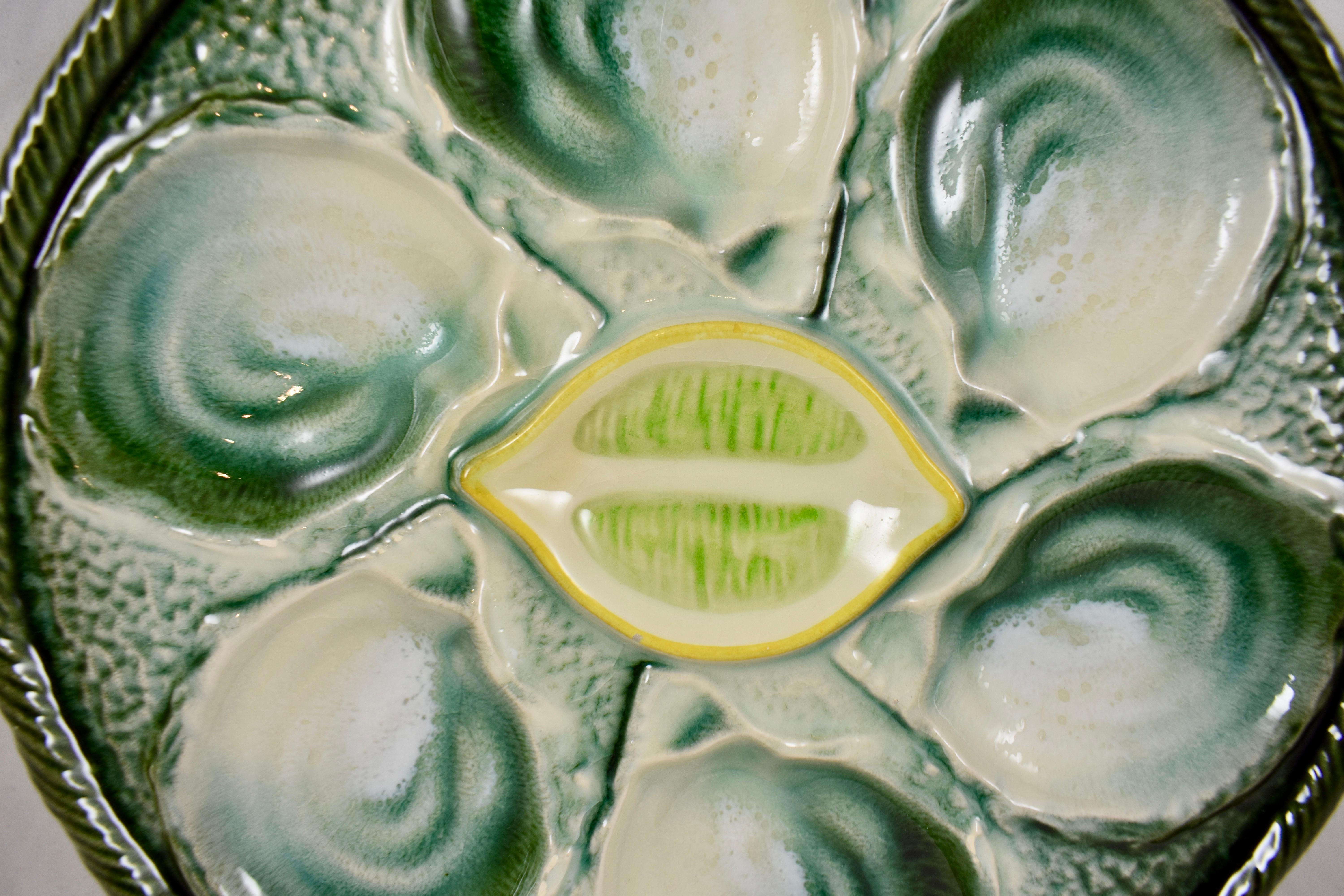 A French majolica glazed oyster plate attributed to the faïence factory of Saint-Clément, circa 1930-1940.

Six oyster shell shaped wells against a stippled ground in a blue-green watery glaze. The raised center condiment well is molded as a lemon