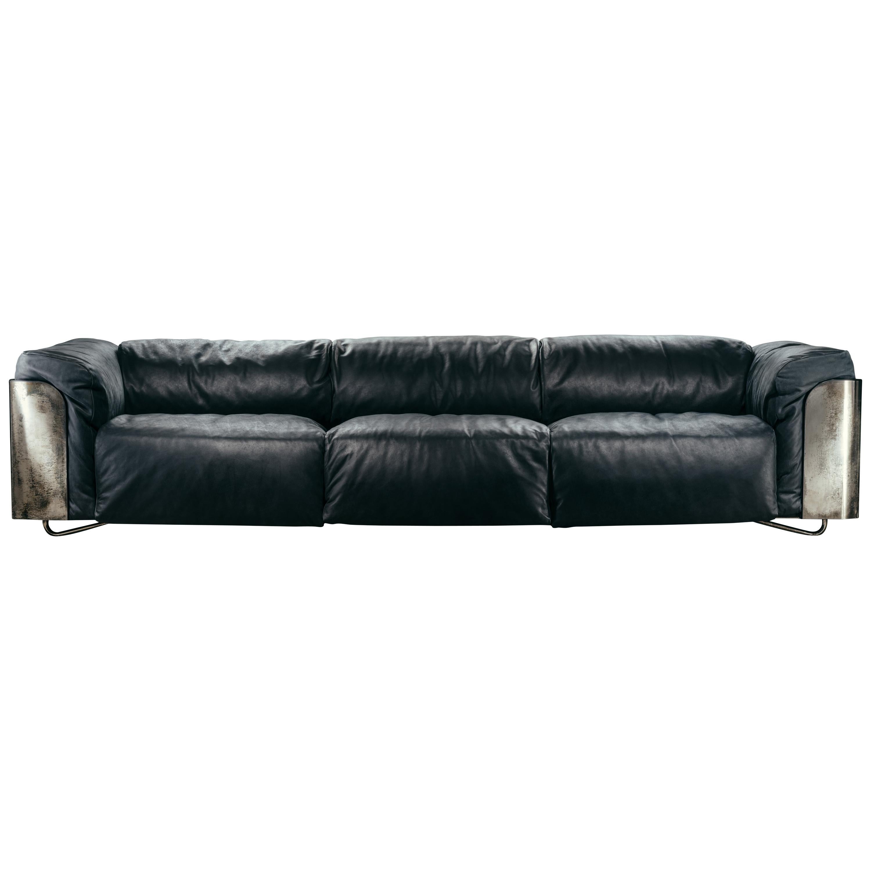 Saint-germain sofa, available in 2 or 3-seater versions, is composed of a matt black wood panel, covered in the external part with a metal plating, with a padded border in the same upholstery of the seating, otherwise in matte black wood. The