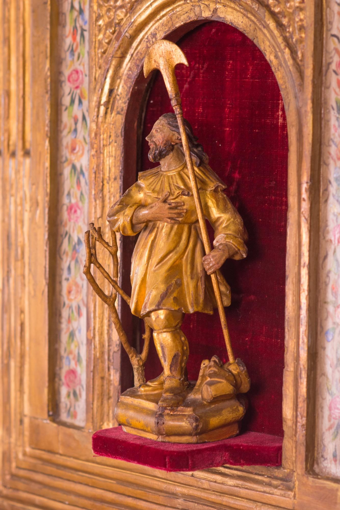 Spanische geschnitzte und polychromierte Skulptur und Altar des Heiligen Isidor, Schutzpatron der Landwirtschaft und des Gartenbaus, aus dem 16. Er steht in einer mit rotem Samt ausgekleideten Nische. Der Altar ist mit gemalten floralen Motiven und