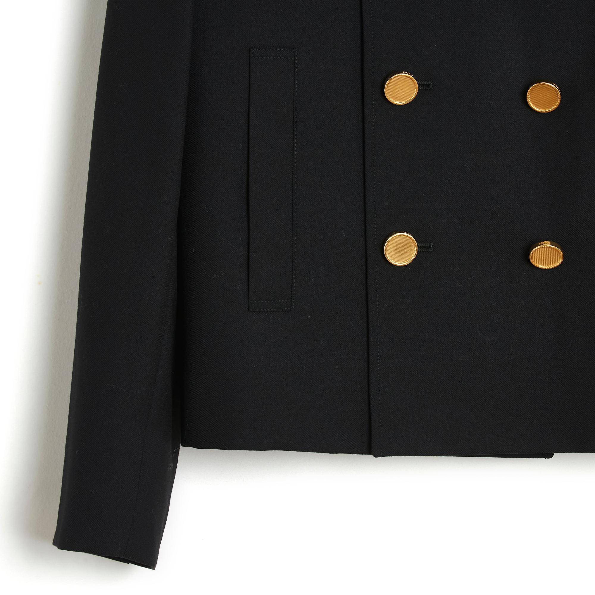 Saint Laurent jacket by Hedi Slimane circa 2013, straight and short cut in black wool cloth, notched collar closed with 6 crossed gold metal buttons, 2 slit pockets at the front, long sleeves closed with 5 jeweled buttons, satin canvas lining black.