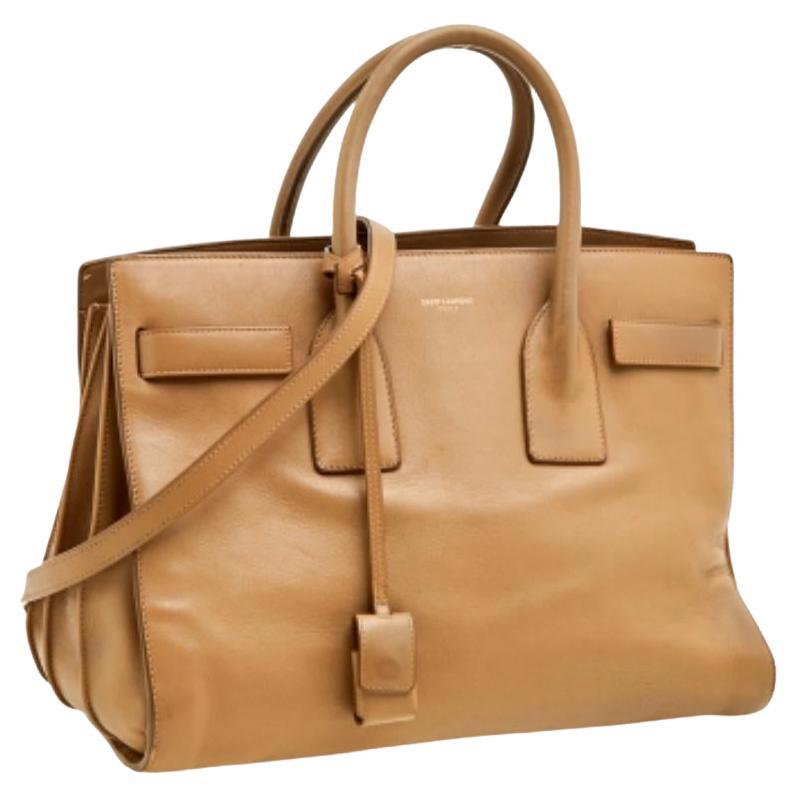This Sac de Jour tote by Saint Laurent has a structure that simply spells sophistication. Crafted from beige leather, the bag is held by double top handles. The tote comes with a suede-lined interior with enough space to store your necessities and