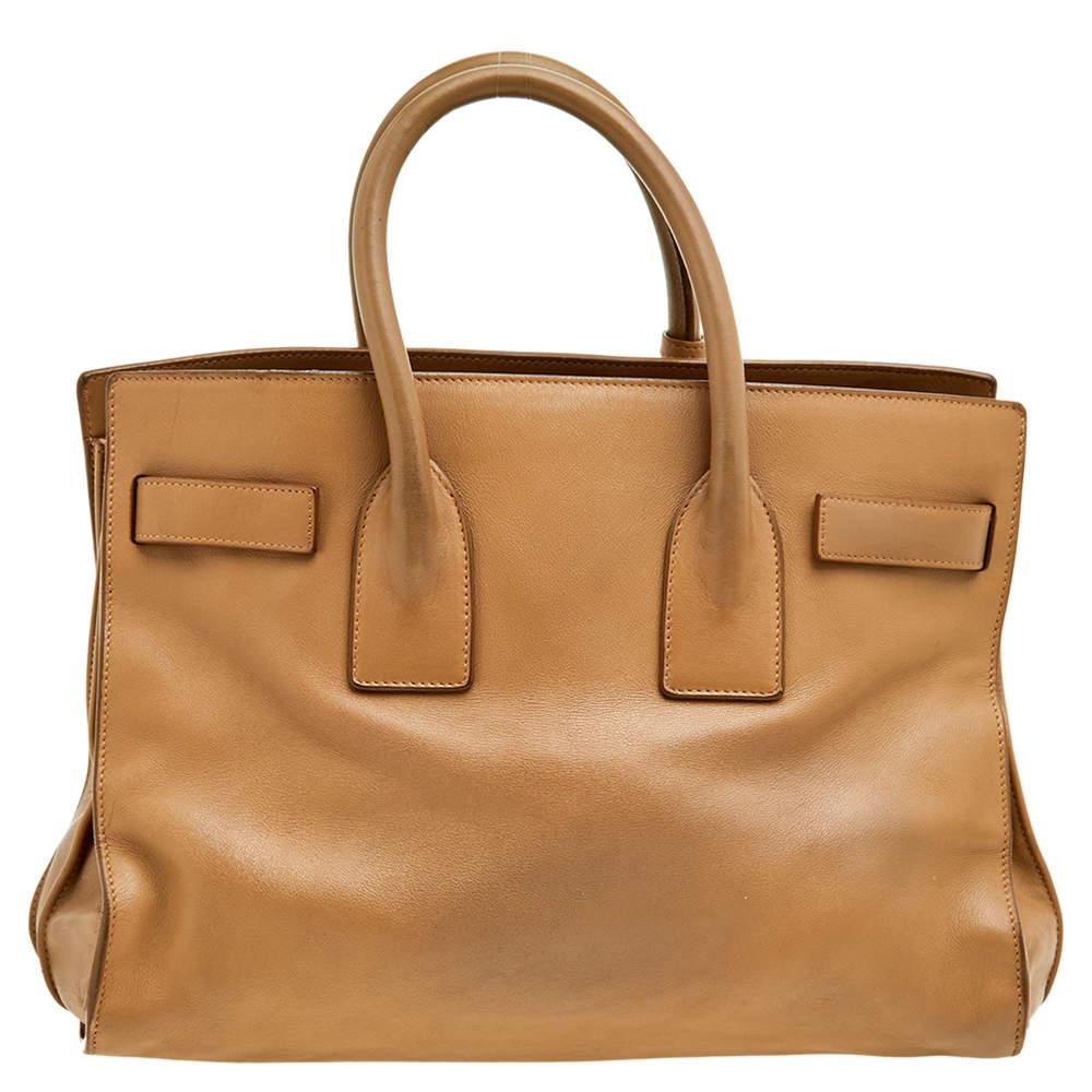 Ce sac à main Sac de Jour de Saint Laurent a une structure qui est tout simplement synonyme de sophistication. Confectionné en cuir beige, le sac est maintenu par une double anse supérieure. Le fourre-tout est doté d'un intérieur doublé en suédine