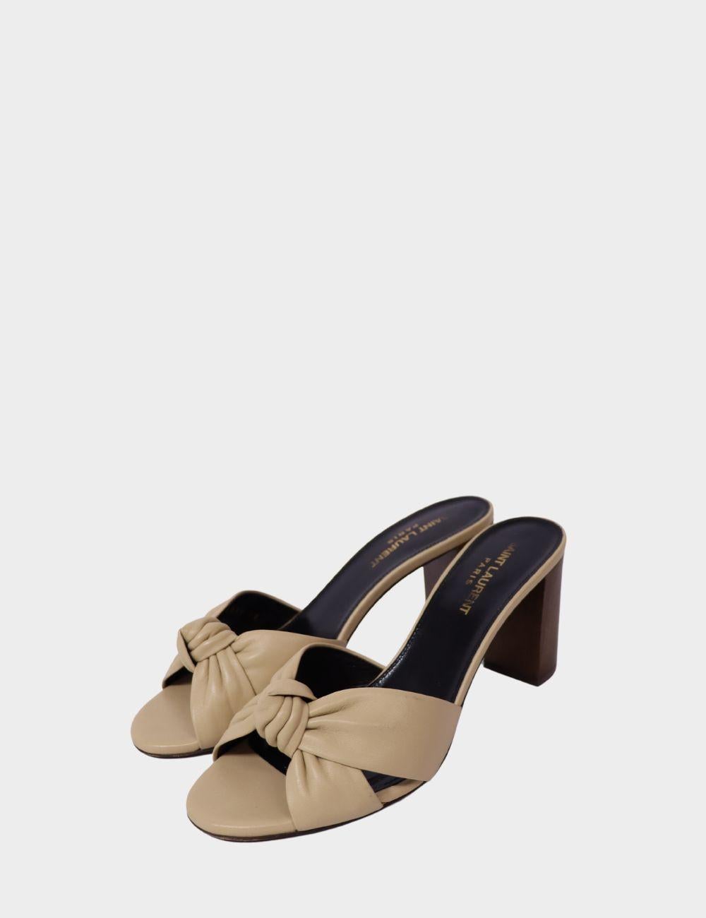 Elevate your step with these Saint Laurent Paris beige leather mules, crafted with a knotted front strap and set on a sturdy block heel. Designed for both comfort and chic appeal, these open-toe heels feature a slip-on silhouette, making them the