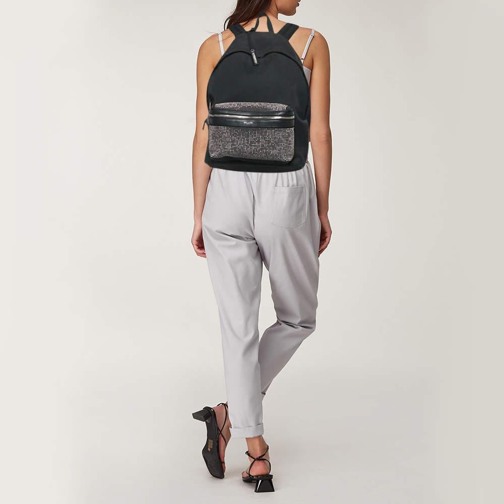 Crafted from durable black canvas and leather  this Saint Laurent backpack features eye catching stud details that add a touch of rock and roll flair. With a spacious interior  it provides ample room for all your essentials while maintaining a sleek
