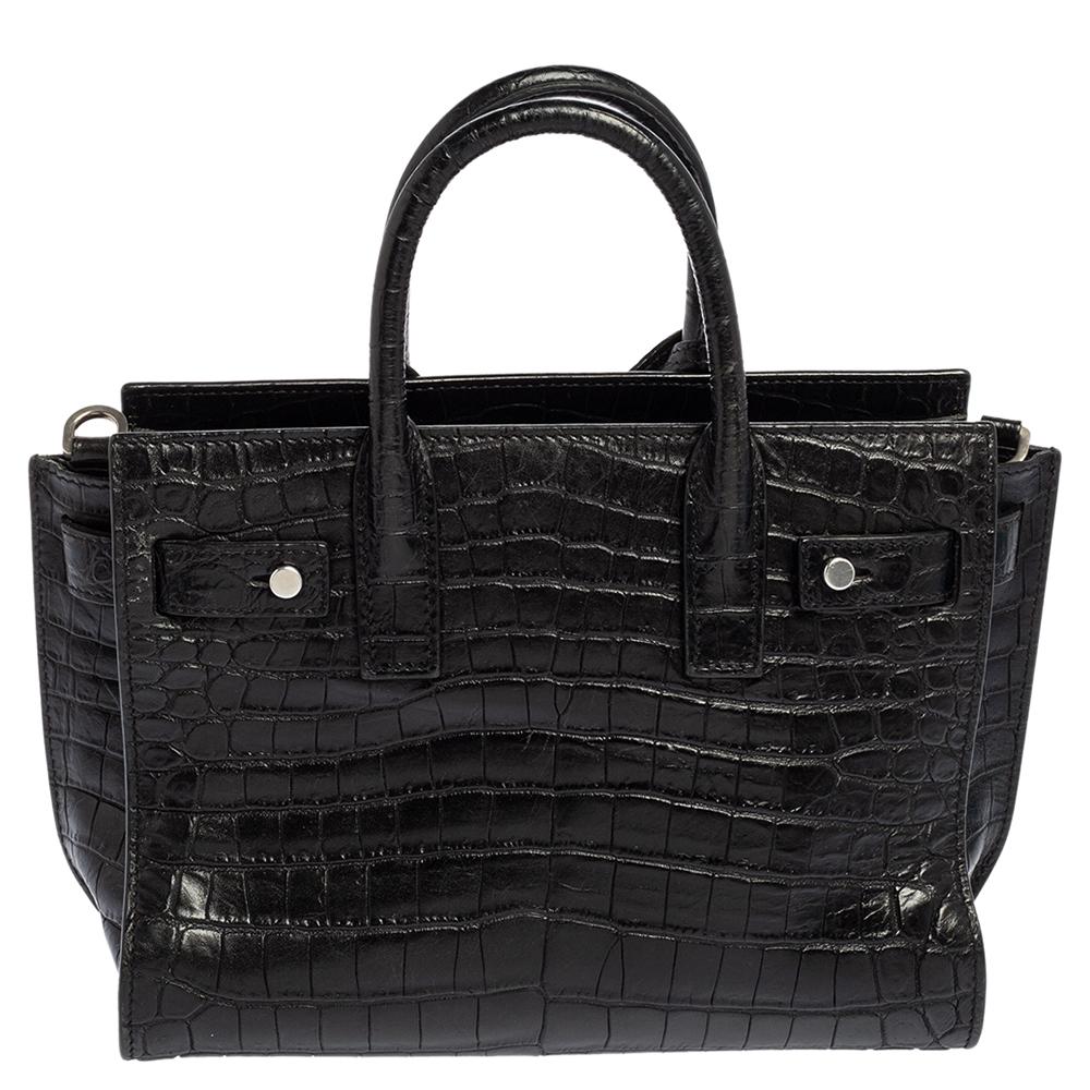 This Nano Classic Sac de Jour tote by Saint Laurent has a structure that exhibits a sophisticated image. Crafted from croc-embossed leather, the bag is held by double top handles and a shoulder strap. The tote comes with a lined interior.

Includes: