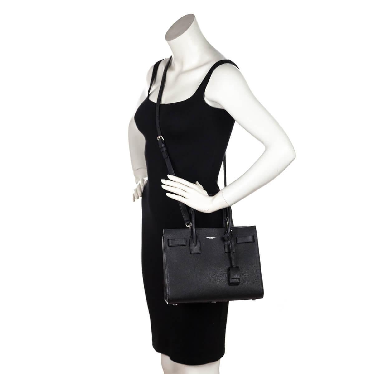 This small tote is made of textured calfskin leather in black. The bag features dual rolled leather top handles and an optional shoulder strap with side short straps that can be undone to increase the width of the bag. The top is open to a matching