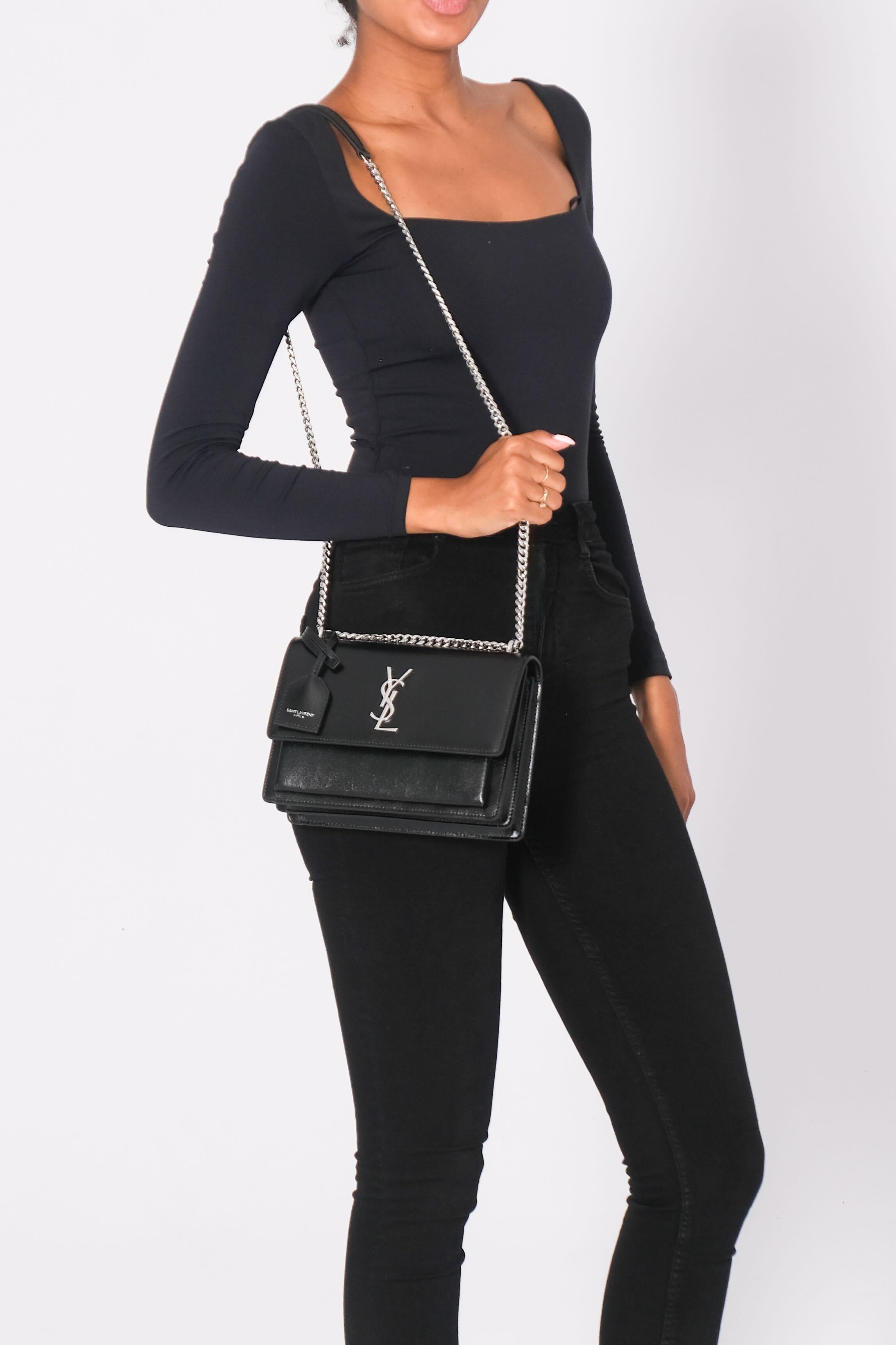Black 'Sunset Medium’ shoulder bag from Saint Laurent. Crafted from calf leather, this design secures with a magnetic snap and showcases metal YSL initials on the front, a slip pocket on the back, a chain-reinforced shoulder strap, antiqued