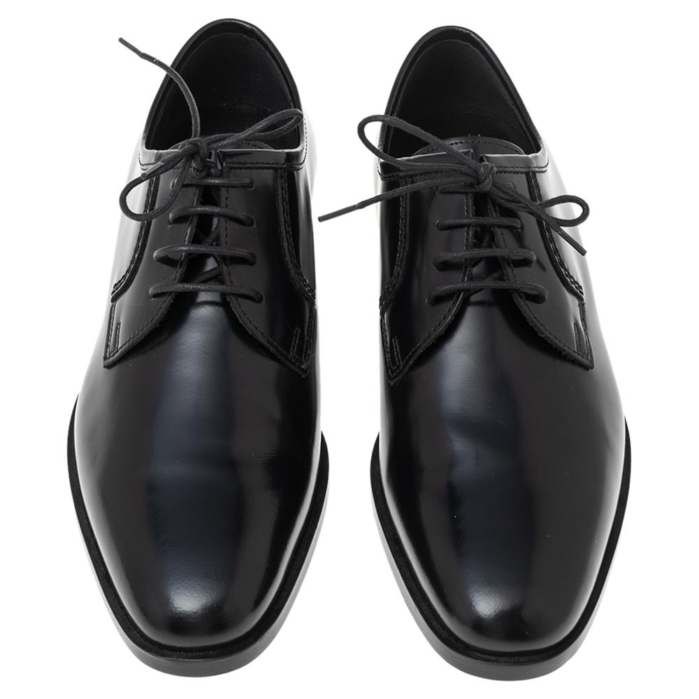 Elevate your formal outfit with this pair of Saint Laurent black derby. Made from leather into a sleek and sharp silhouette, the it is styled with lace-up vamps and exhibits a shiny look. The brand detailing on the side of low heels gives the shoes