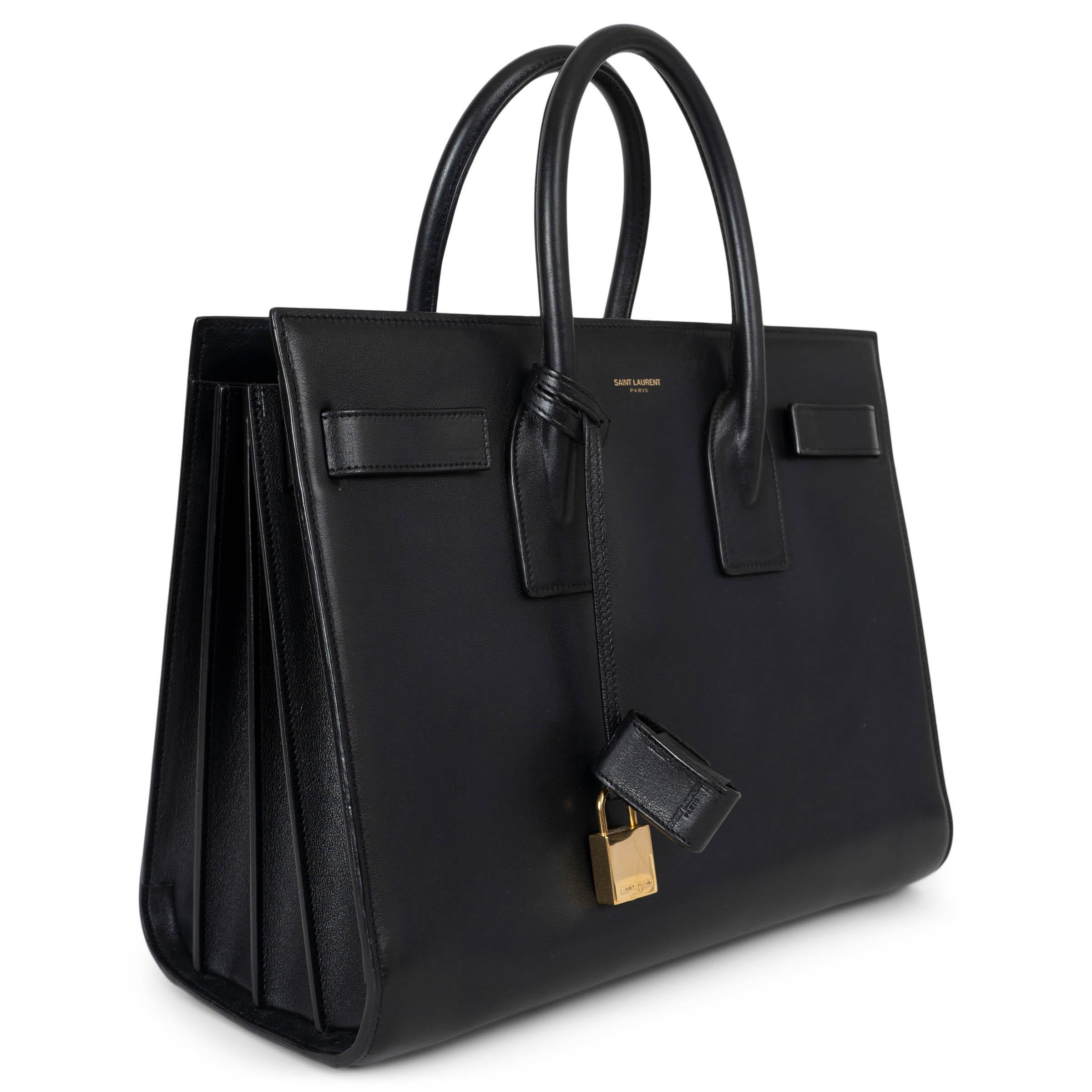 This 100% authentic Saint Laurent Sac de Jour bag in its iconic size is a timeless symbol of elegance and functionality. Crafted in smooth black calfskin with a spacious, suede-lined interior, it features two compartments separated by a zipped