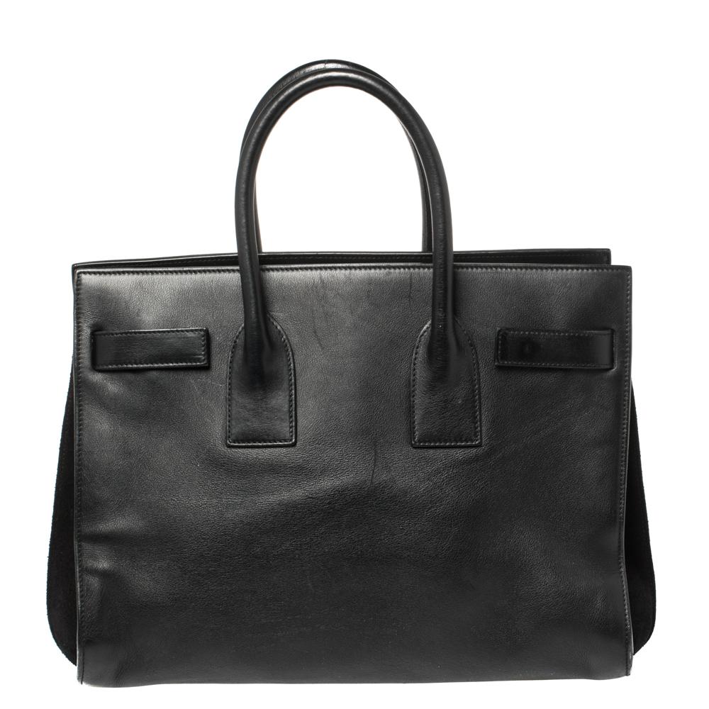 This Sac de Jour tote by Saint Laurent has a structure that simply spells sophistication. Crafted from black leather, the bag is held by double top handles. The tote comes with a suede-lined interior with enough space to store your necessities and