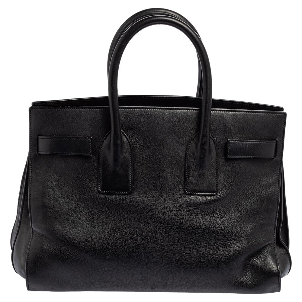 This Sac de Jour tote by Saint Laurent has a structure that simply spells sophistication. Crafted from black leather, the bag is held by double top handles. The tote comes with a suede-lined interior with enough space to store your necessities and