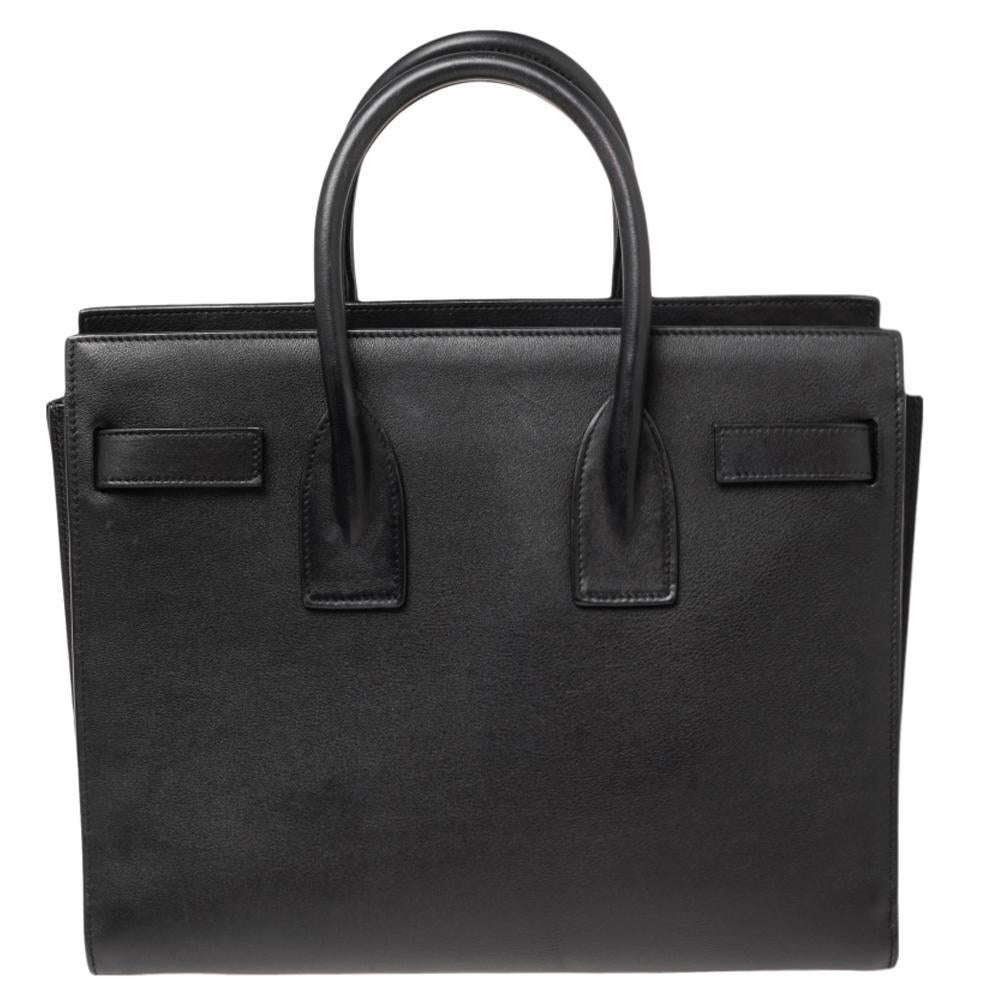 This Sac de Jour tote by Saint Laurent has a structure that simply spells sophistication. Crafted from black leather, the bag is held by double top handles. The tote comes with a leather-lined interior with enough space to store your necessities and