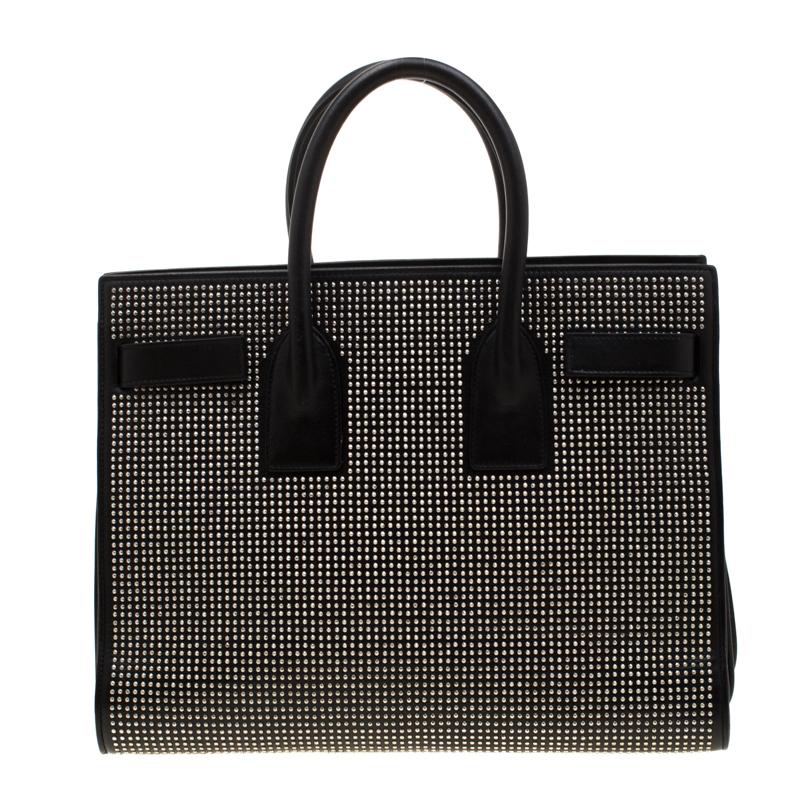 This Sac de Jour tote by Saint Laurent has a structure that simply spells sophistication. Crafted from black leather, the bag is held by double top handles and flaunts a studded exterior. The tote comes with a suede and fabric-lined interior with