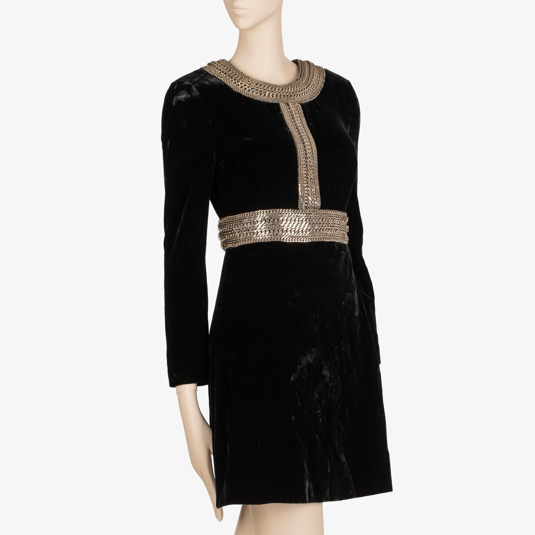 À la fois imposante et raffinée, cette mini robe Saint Laurent allie une texture riche à des ornements sculpturaux. Confectionnée dans un somptueux velours noir, la silhouette est définie par un audacieux travail de chaînage argenté : un collier à