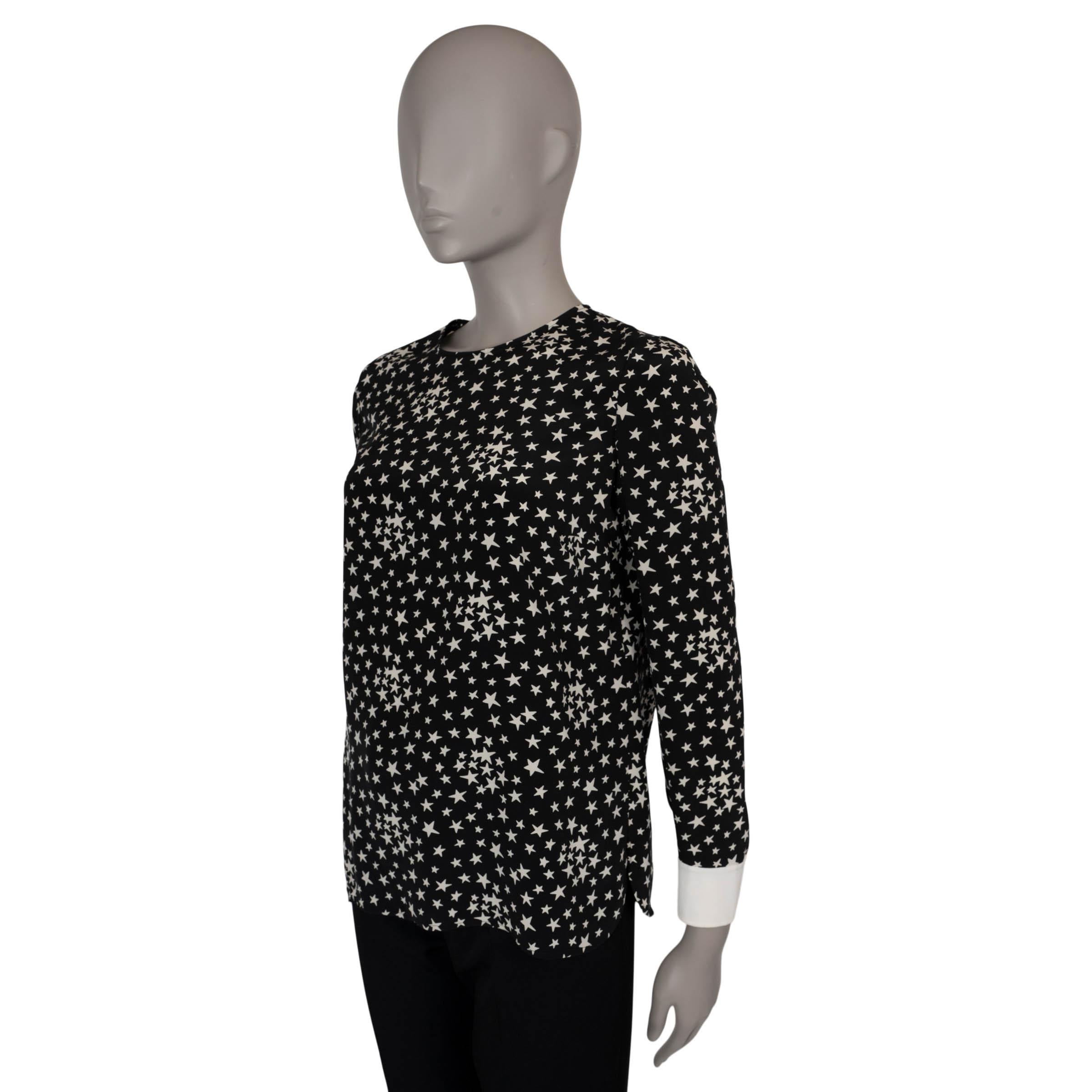 This 100% authentic Saint Laurent blouse in black silk (100%) features an allover white star print, offering a playful yet sophisticated look. It has a round neck and contrasting white cuffs adorned with fabric-covered buttons, adding a refined