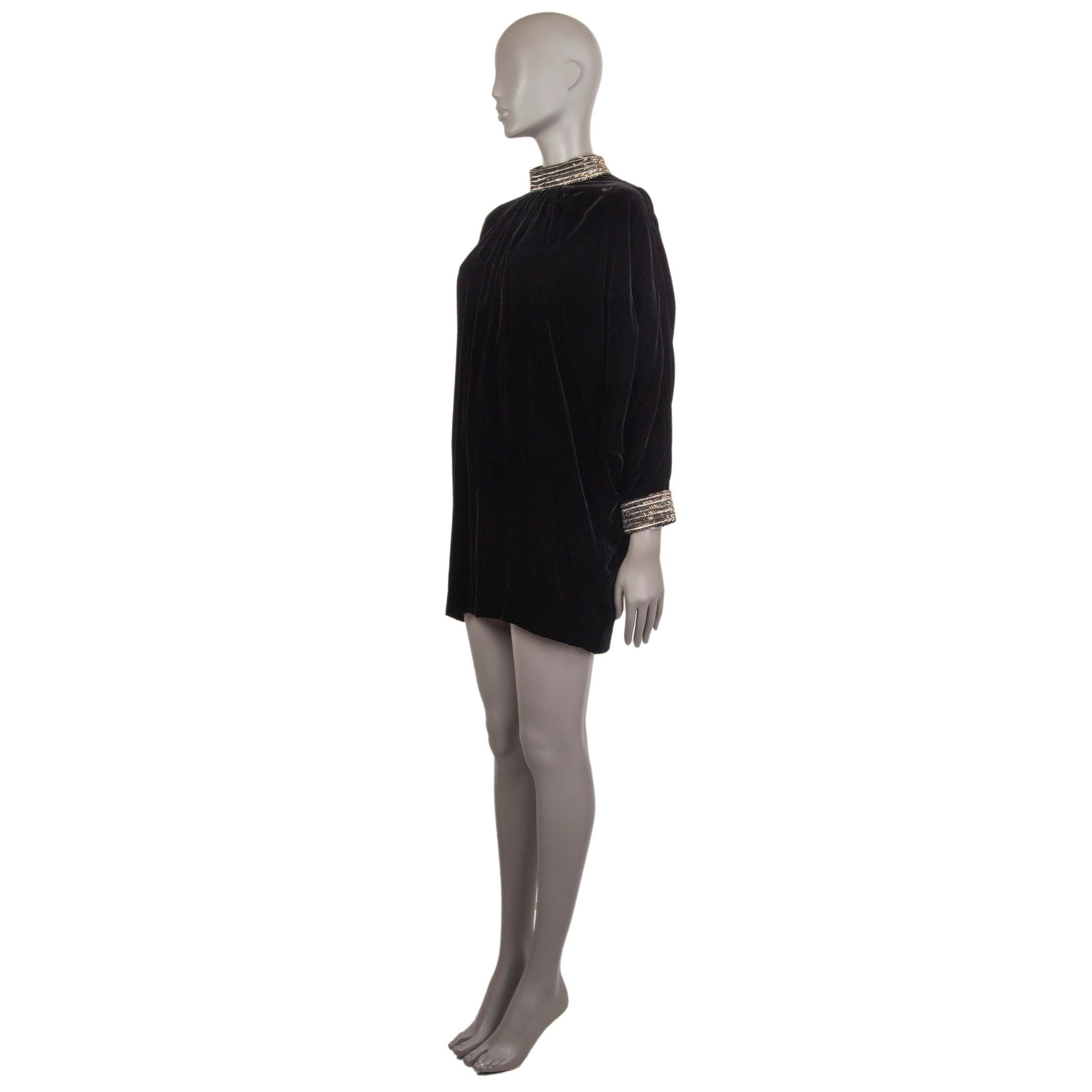 Saint Laurent velvet mini dress in black viscose (78%) and silk (22%). With beaded mock neck and cuffs, pleats falling from the neckline, and batwing sleeves. Closes with three hooks behind the neck and invisible zipper on the back. Lined in black