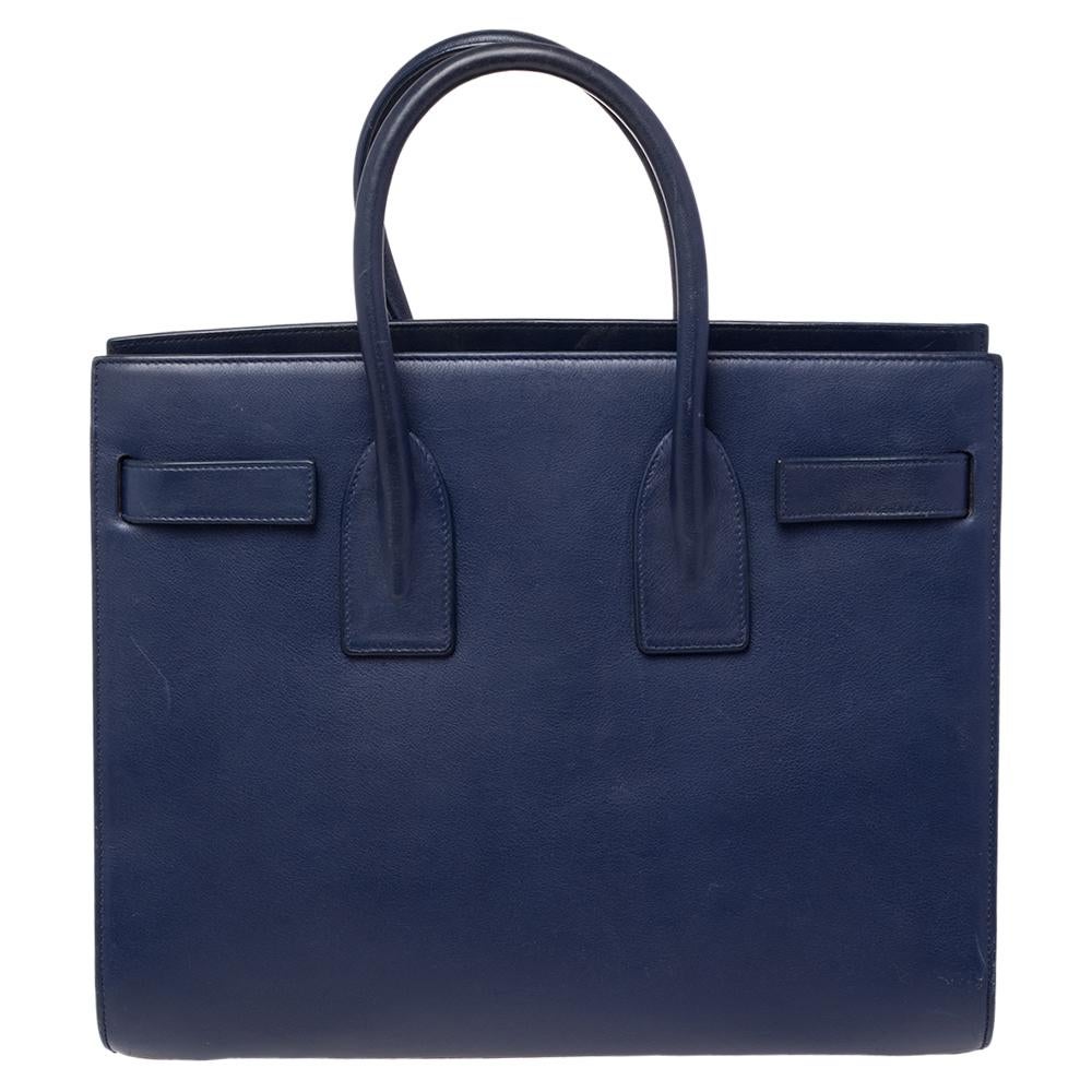 This Sac de Jour tote by Saint Laurent has a structure that simply spells sophistication. Crafted from blue leather, the bag is held by double top handles. The tote comes with a suede-lined interior with enough space to store your necessities and