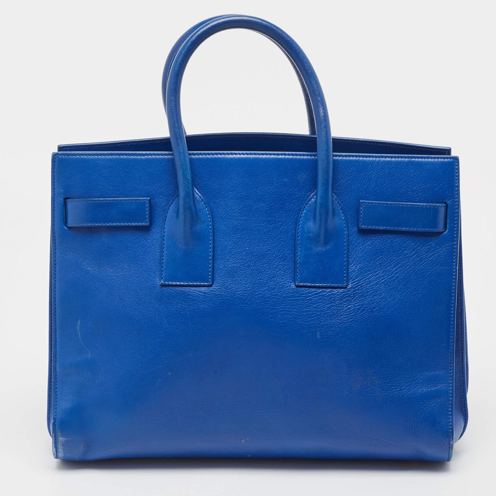 Diese Sac de Jour Tote von Saint Laurent hat eine Struktur, die ein raffiniertes Bild abgibt. Die aus blauem Leder gefertigte Tasche lässt sich durch doppelte obere Griffe und einen Schulterriemen schick tragen. Die Tasche ist mit einem stilvollen