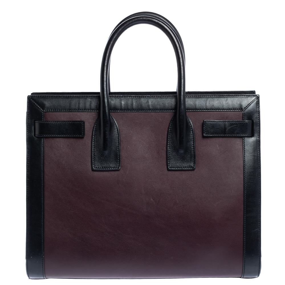 The Sac De Jour tote from Saint Laurent is a timeless creation that is absolutely investment worthy! This burgundy and black tote features a leather construction that employs dual handles at the top and gold-tone protective studs at the bottom. The