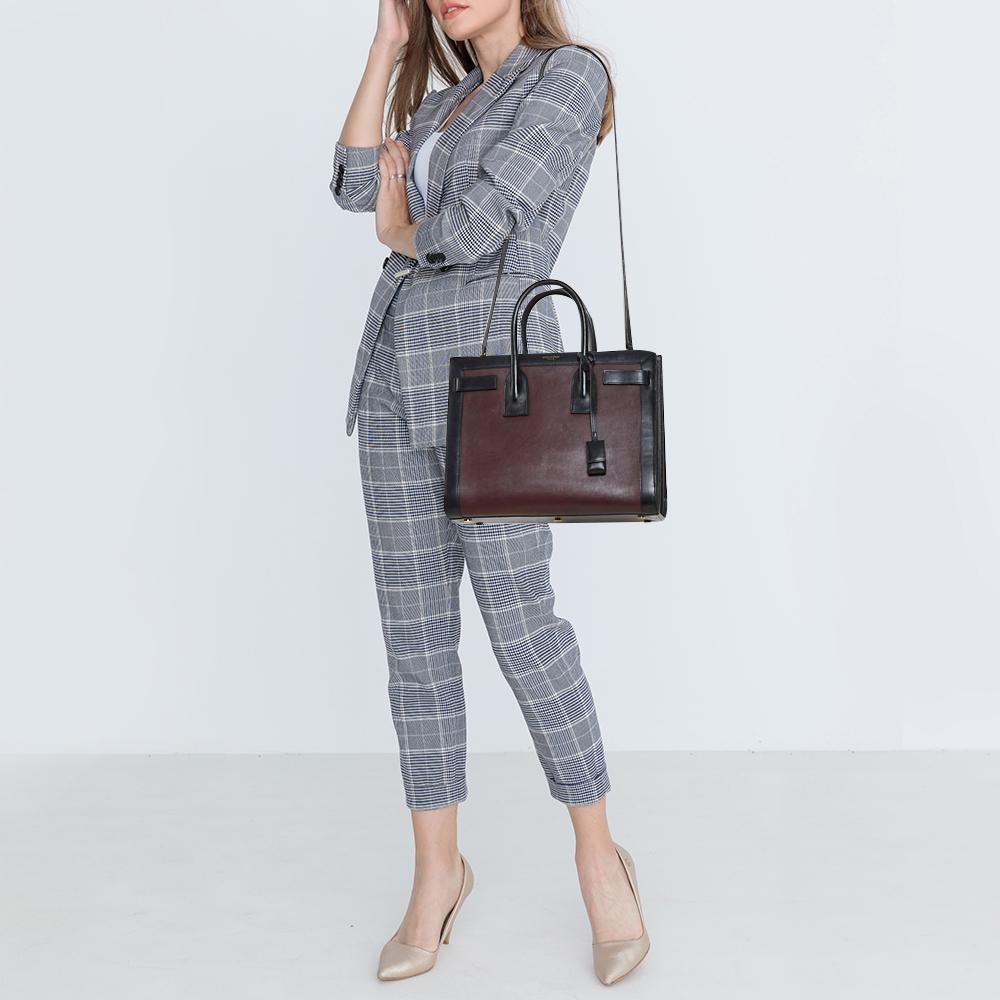 This Sac de Jour tote by Saint Laurent has a structure that simply spells sophistication. Crafted from burgundy & black leather, the bag is held by double top handles. The tote comes with a canvas-lined interior with enough space to store your