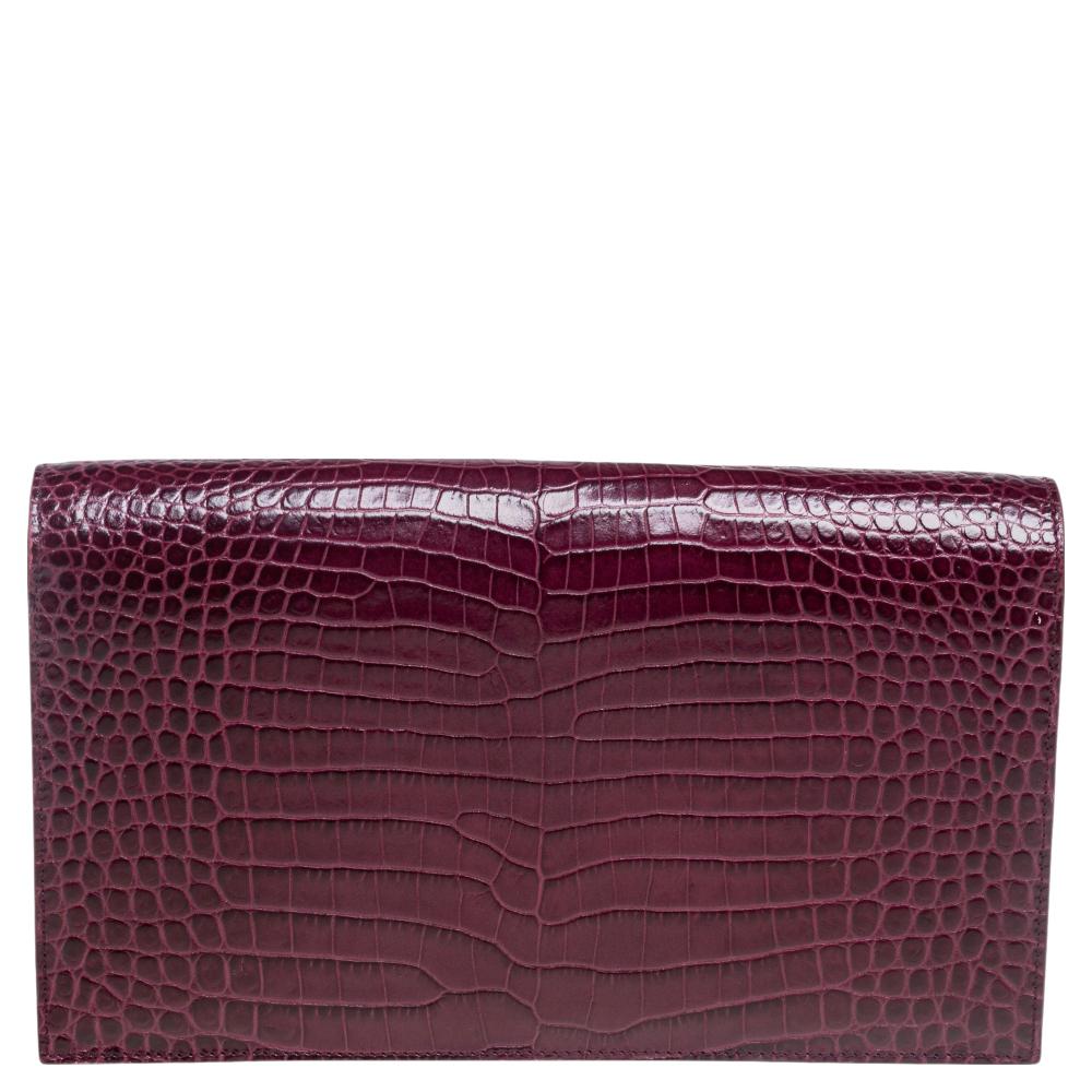 A classic and chic style with a glamorous look to it, this Saint Laurent clutch will take a special place in your collection for years to come. Crafted in burgundy croc-embossed leather and accented with gold-tone YSL monogram detail at the front