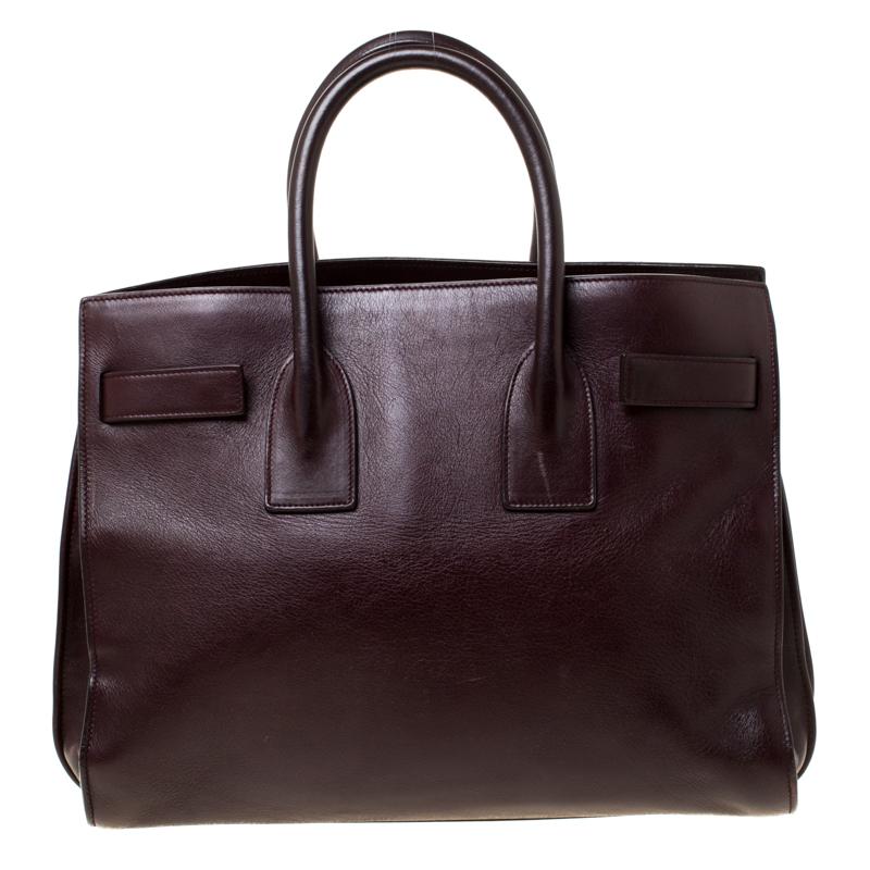 This Sac de Jour tote by Saint Laurent has a structure that simply spells sophistication. Crafted from burgundy leather, the bag is held by double top handles. The tote comes with a suede and fabric-lined interior with enough space to store your