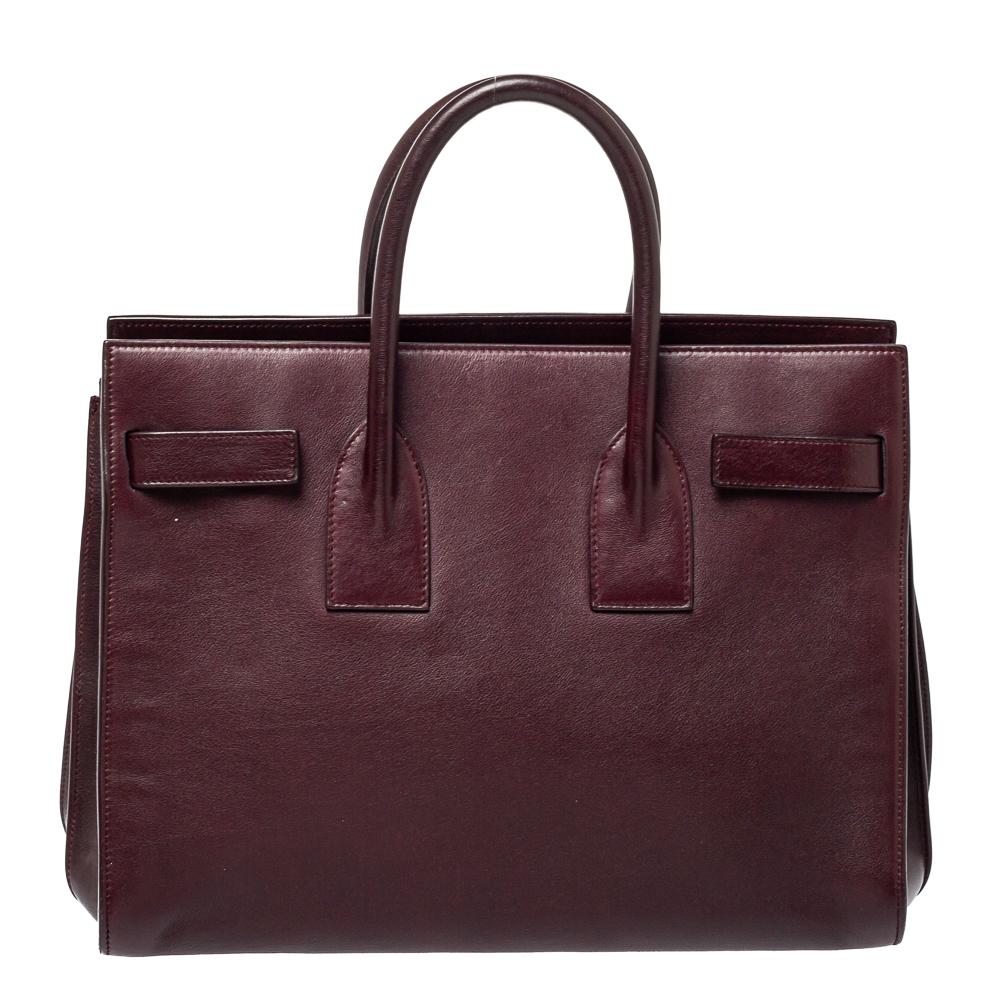 This Sac de Jour tote by Saint Laurent has a structure that simply spells sophistication. Crafted from burgundy leather, the bag is held by double top handles. The tote comes with a suede-lined interior with enough space to store your necessities