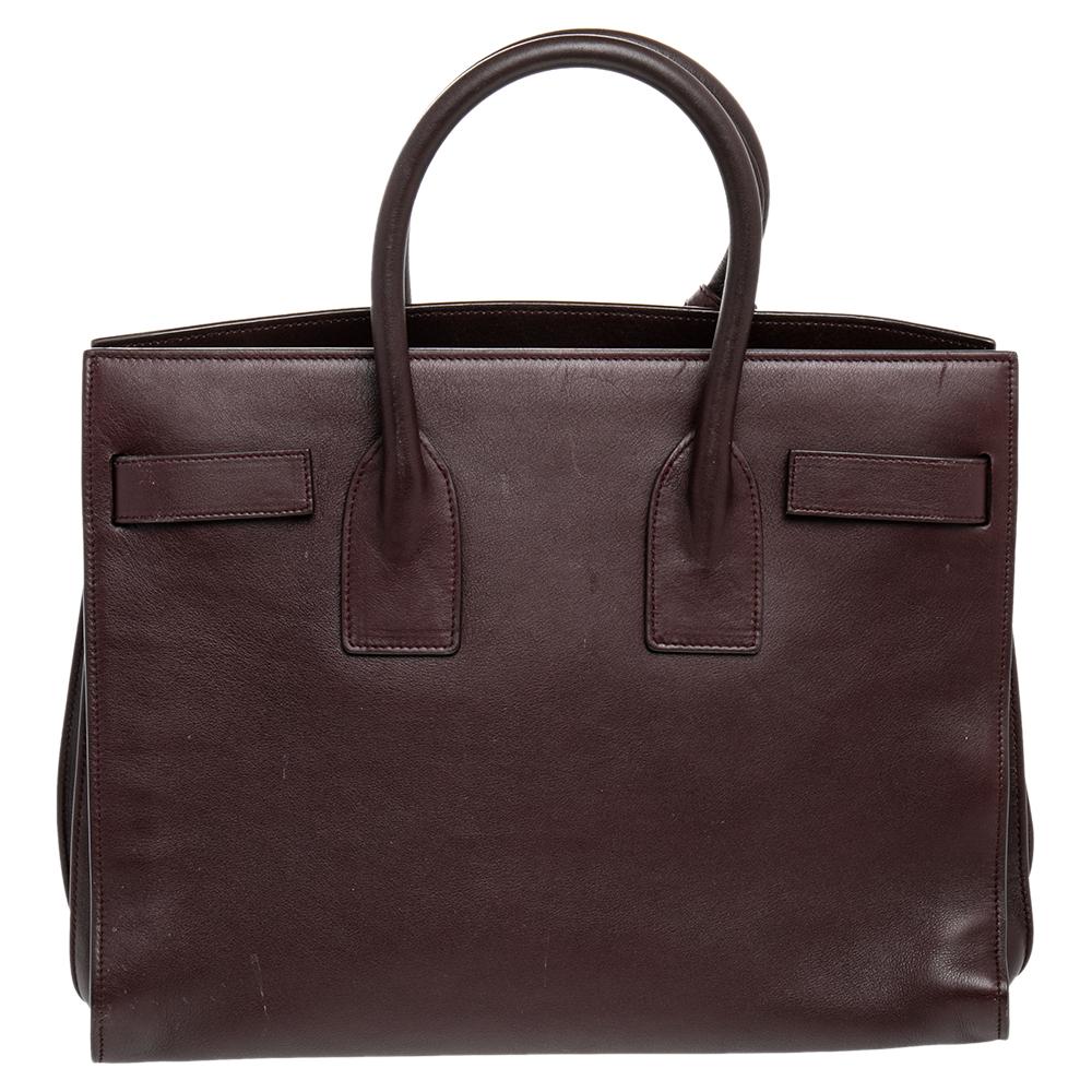 This Sac de Jour tote by Saint Laurent has a structure that simply spells sophistication. Crafted from burgundy leather, the bag is held by double top handles. The tote comes with a suede-lined interior with enough space to store your necessities