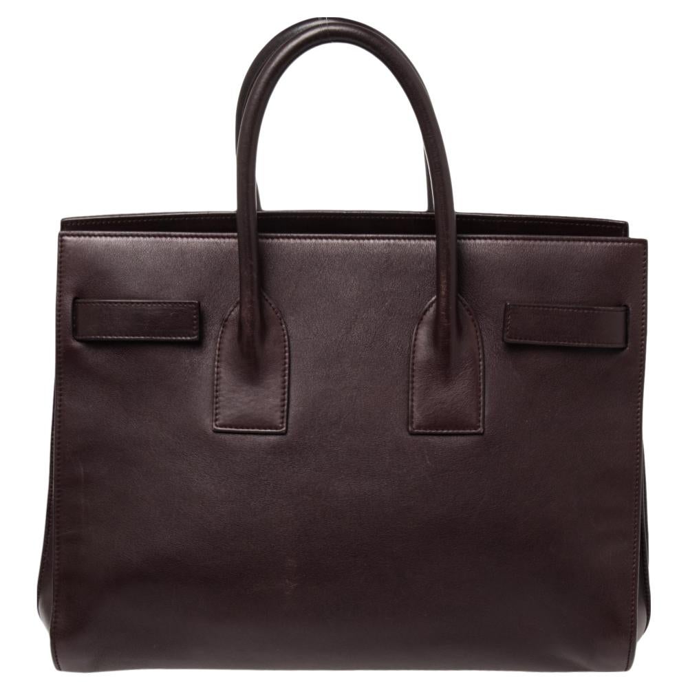 This Sac de Jour tote by Saint Laurent has a structure that simply spells sophistication. Crafted from burgundy leather, the bag is held by double top handles. The tote comes with a suede-lined interior with enough space to store your necessities