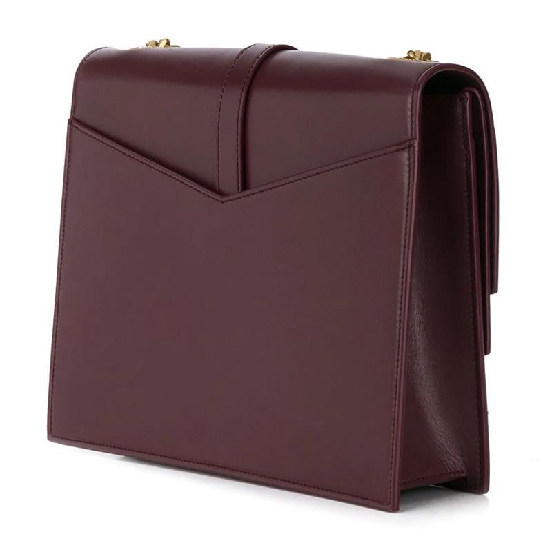 This bag is made with burgundy smooth calf leather and is the medium model. The bag features a triple v-flap, gold tone hardware, a long gourmette (a jewellery chain) shoulder strap, metallic YSL logo on front flap and black interior lining with