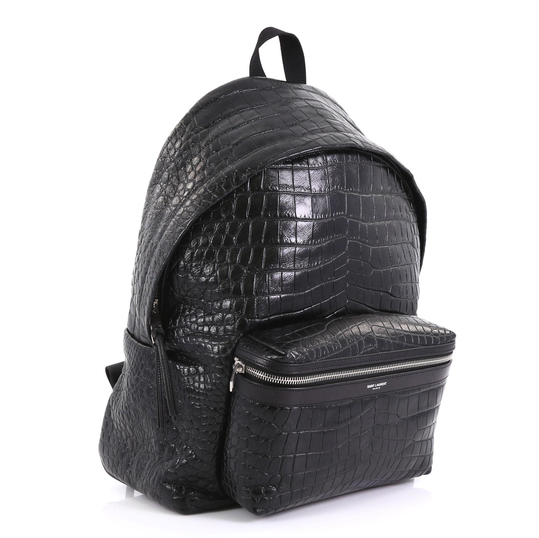 This Saint Laurent City Backpack Crocodile Embossed Leather Medium, crafted from black crocodile embossed leather, features adjustable padded straps, exterior front zip pocket, and silver-tone hardware. Its two-way zip closure opens to a black