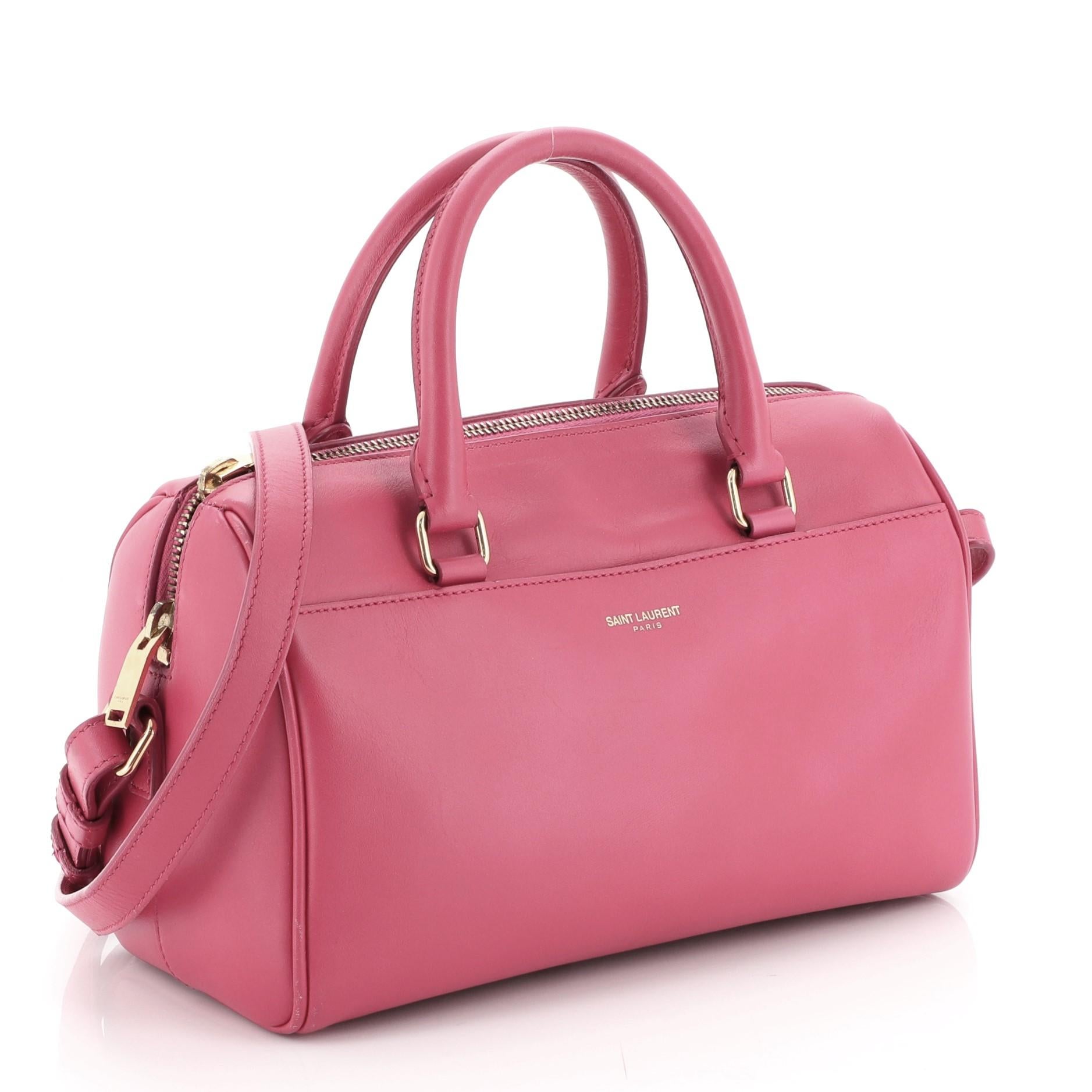 This Saint Laurent Classic Baby Duffle Bag Leather, crafted from pink leather, features dual rolled handles, protective base studs, and gold-tone hardware. Its two-way zip closure opens to a pink suede interior with side slip pocket. 

Estimated