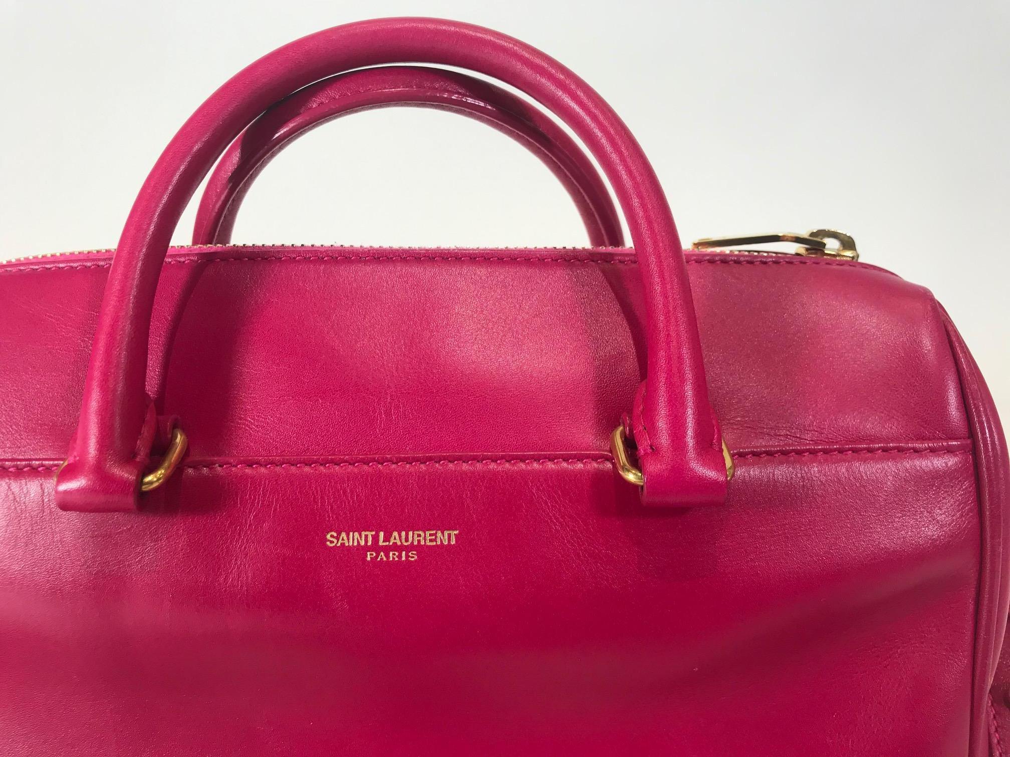 Pink leather. Gold-tone hardware. Zip closure at top. Dual rolled top handles. Single flat shoulder strap. Single slit pocket at front. Tonal suede lining. Single zip pocket at interior wall.