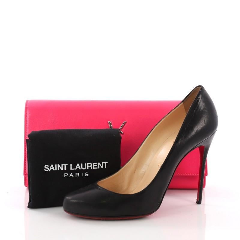 This Saint Laurent Classic Monogram Clutch Leather Long, crafted in pink leather, features YSL logo and silver-tone hardware. Its magnetic snap closure opens to a black fabric interior with slip pocket. **Note: Shoe photographed is used as a sizing