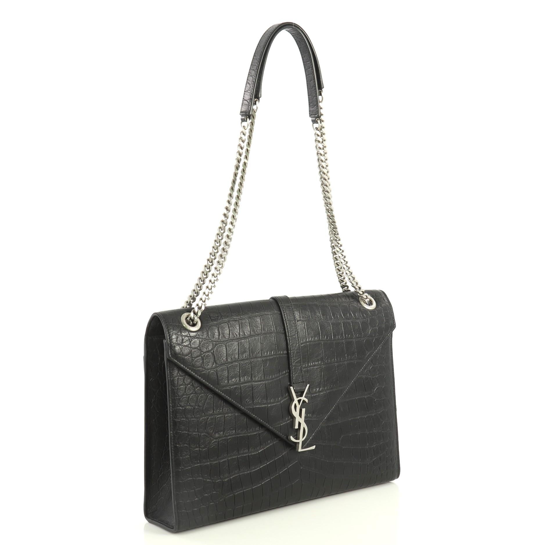 This Saint Laurent Classic Monogram Envelope Satchel Crocodile Embossed Leather Large, crafted from black crocodile embossed leather, features chain link straps with leather pads, YSL monogram logo at the front, and aged silver-tone hardware. Its