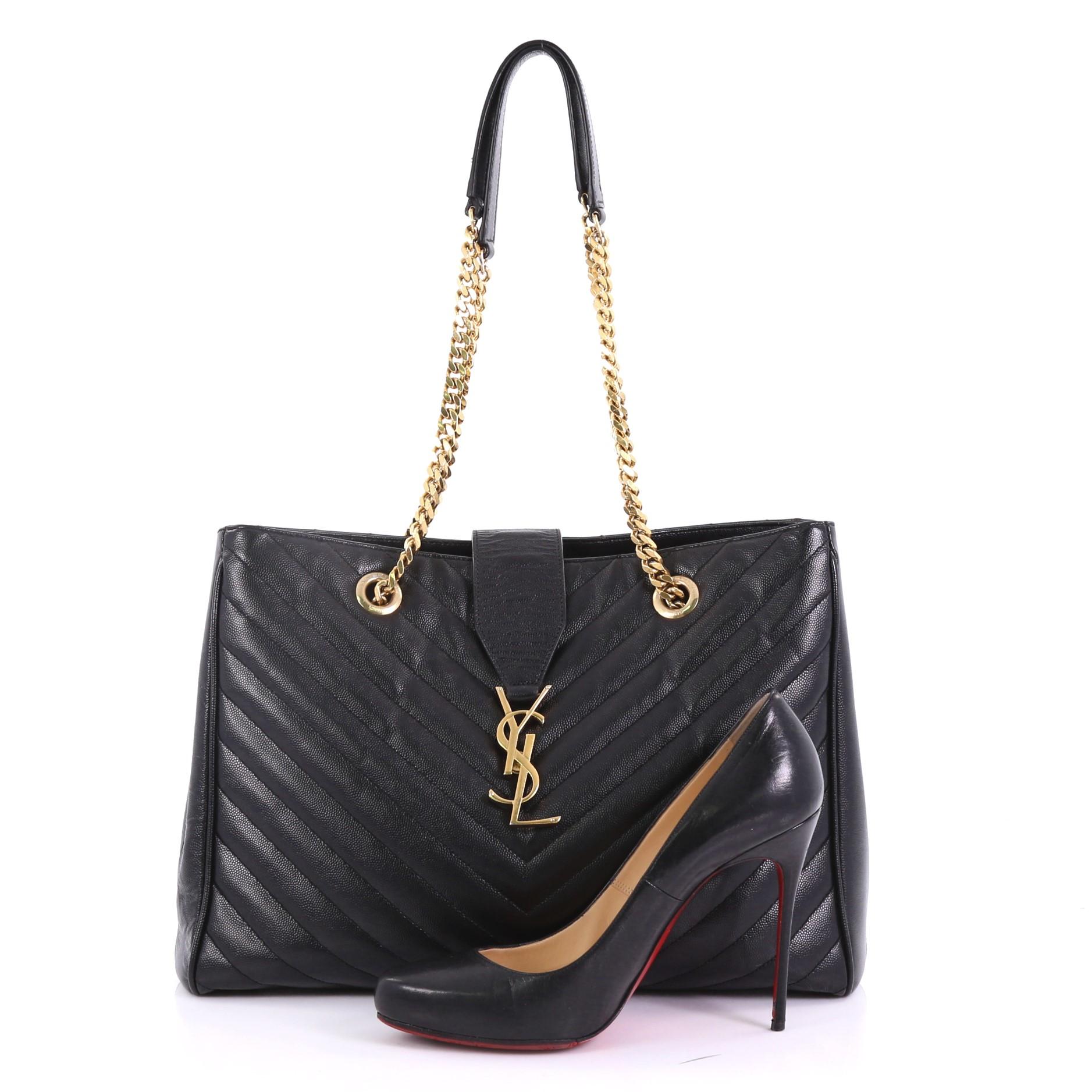 This Saint Laurent Classic Monogram Shopper Matelasse Chevron Leather Large, crafted from black matelasse chevron leather, features dual grommet chain straps with leather pads, YSL logo at the front, and gold-tone hardware. It opens to a black
